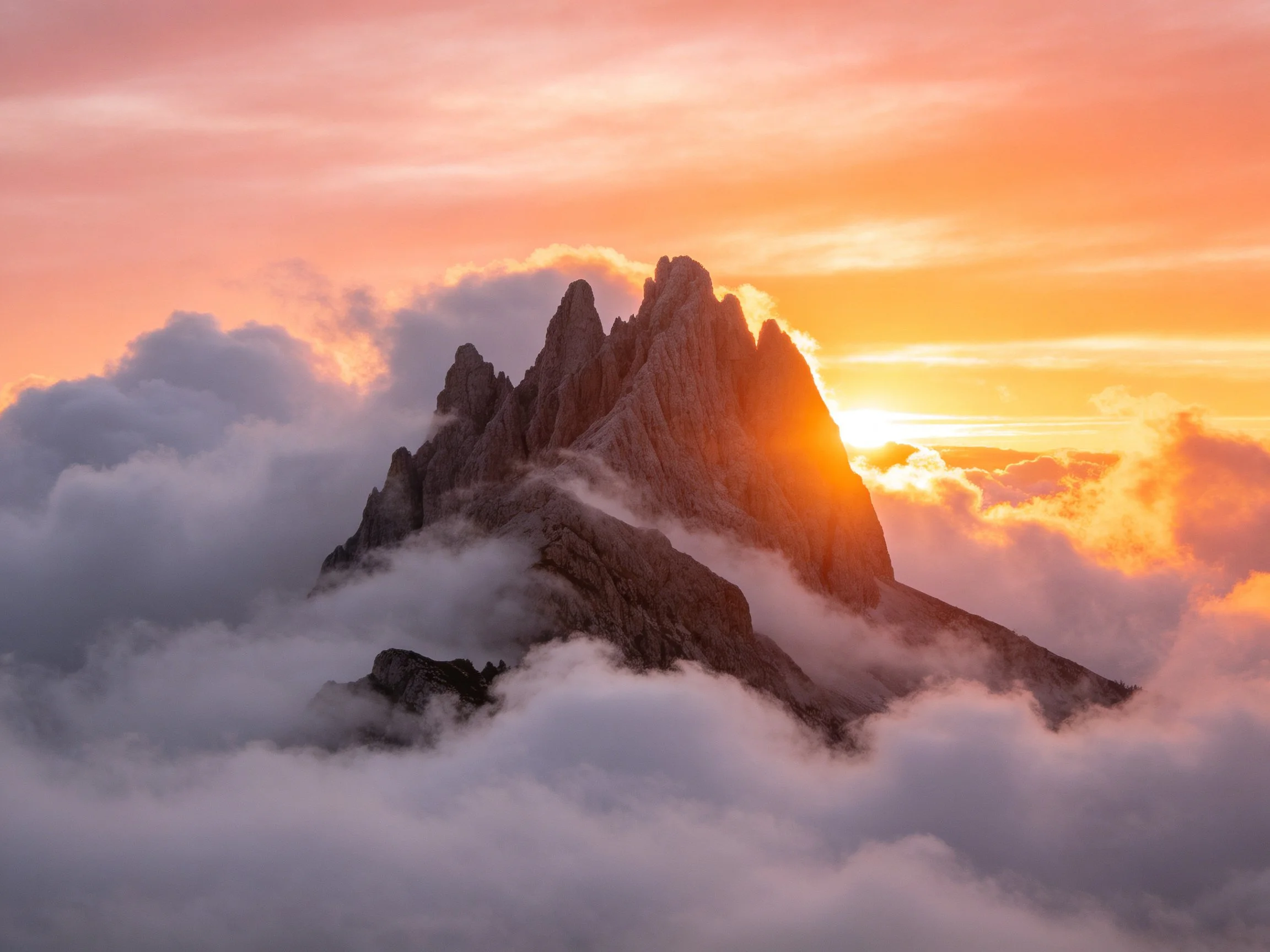 Sunset illuminates jagged mountain peaks amid swirling clouds