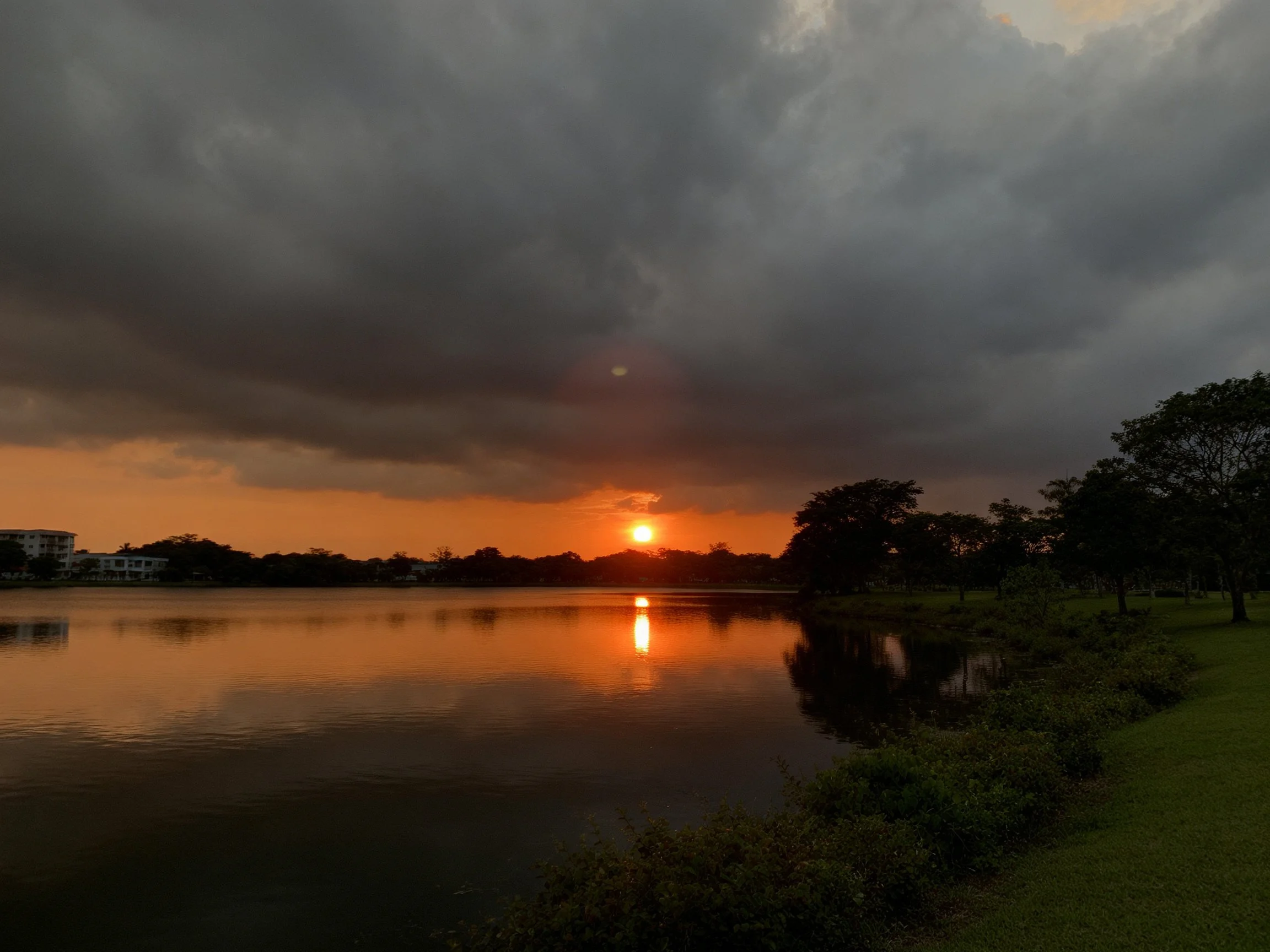 Sunset over calm lake with dark stormy clouds and orange horizon