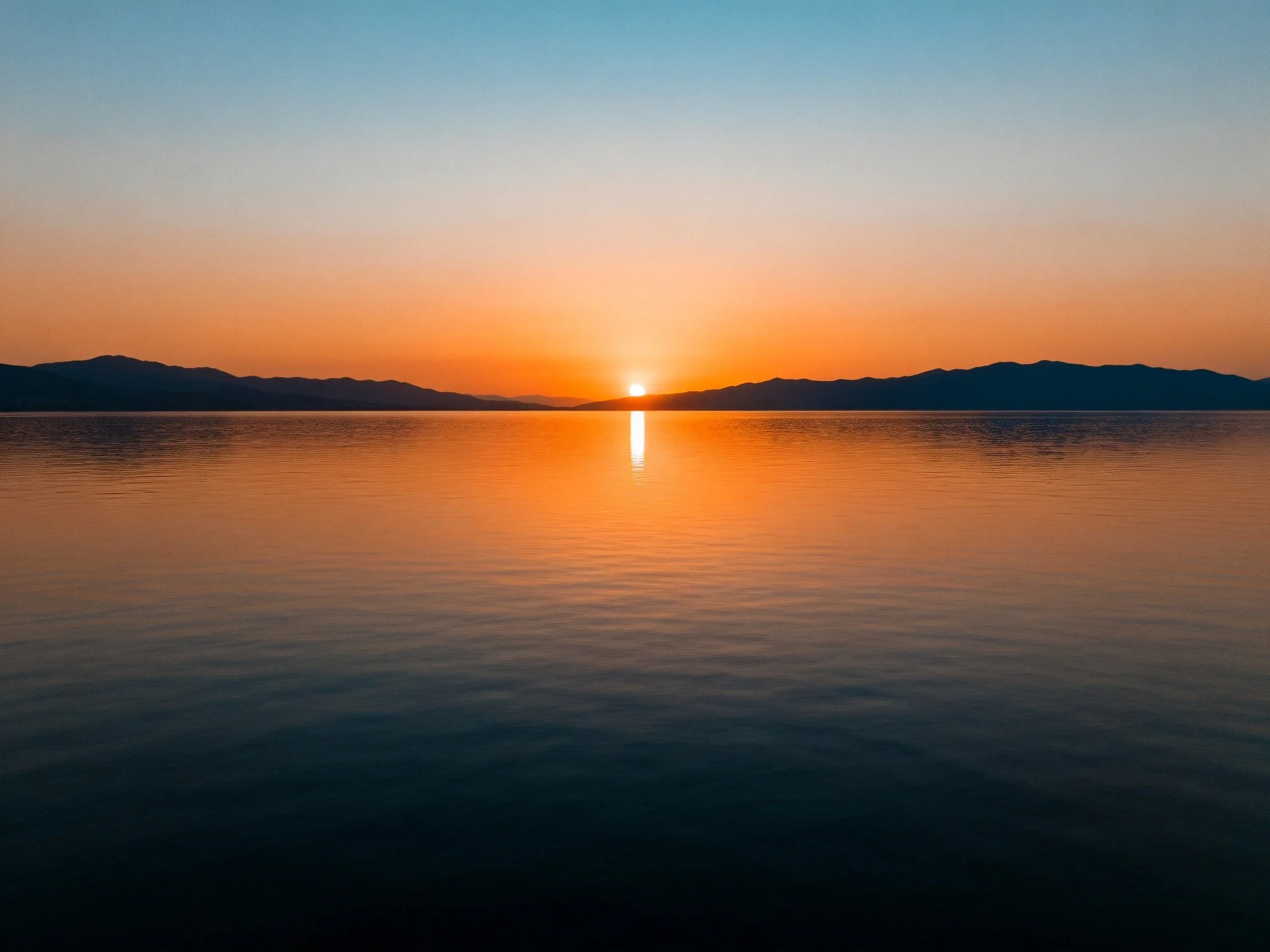 Sunset over calm lake with orange sky and mountain silhouettes