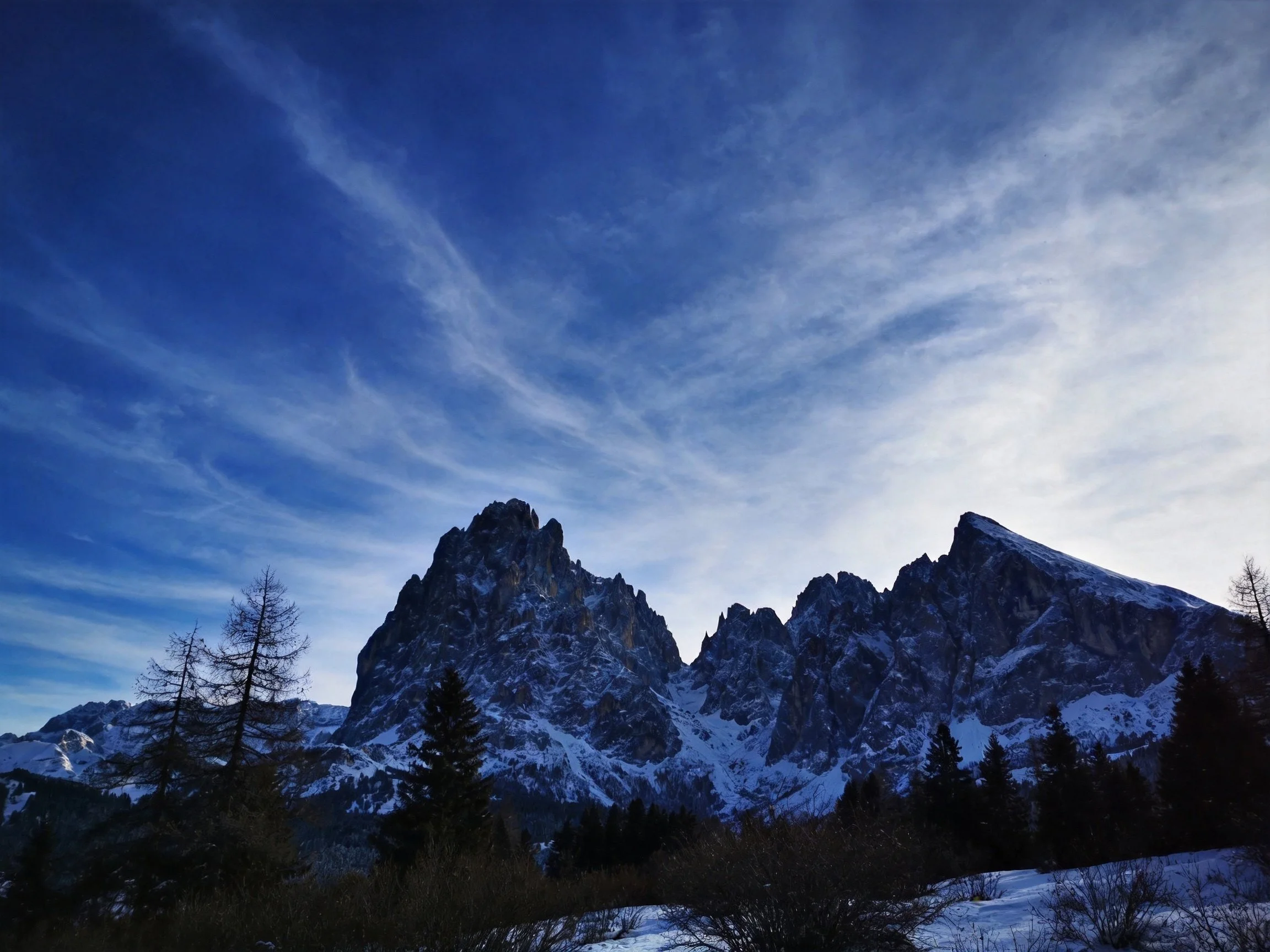 Tall snow-covered mountain peaks beneath a deep blue sky with wispy clouds
