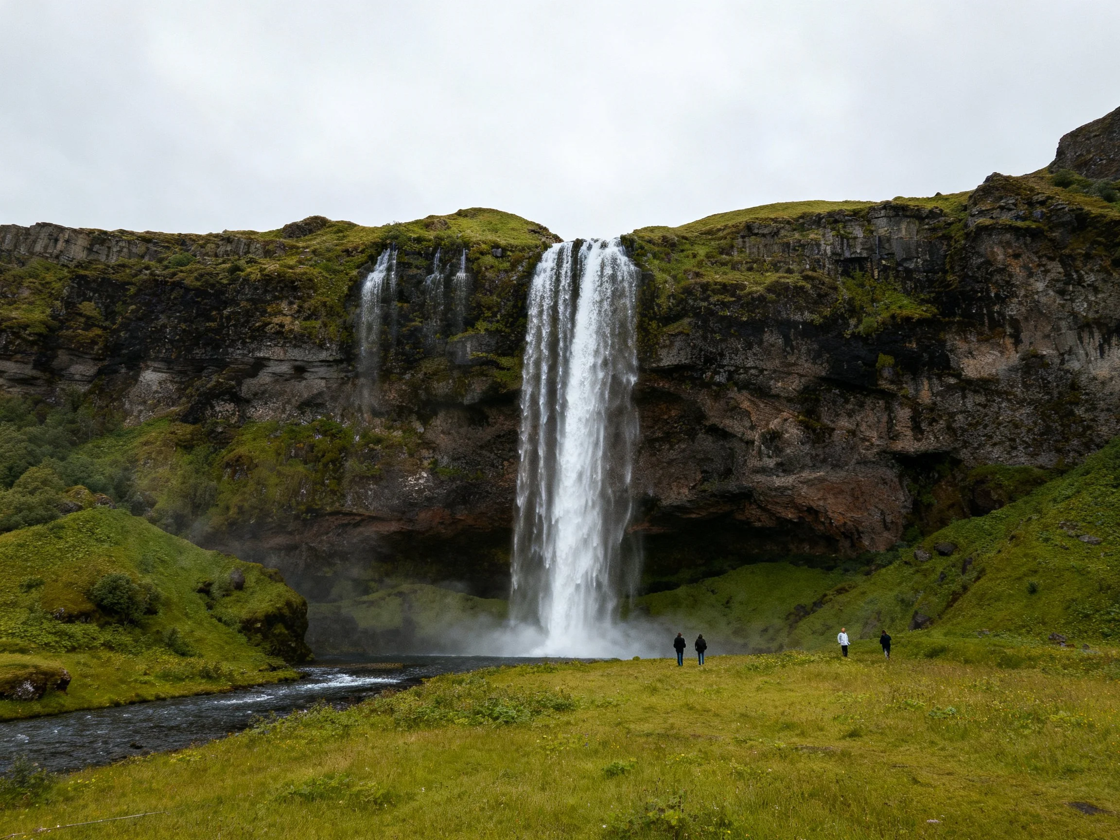 Tall waterfall cascades over mossy cliffs into a misty pool