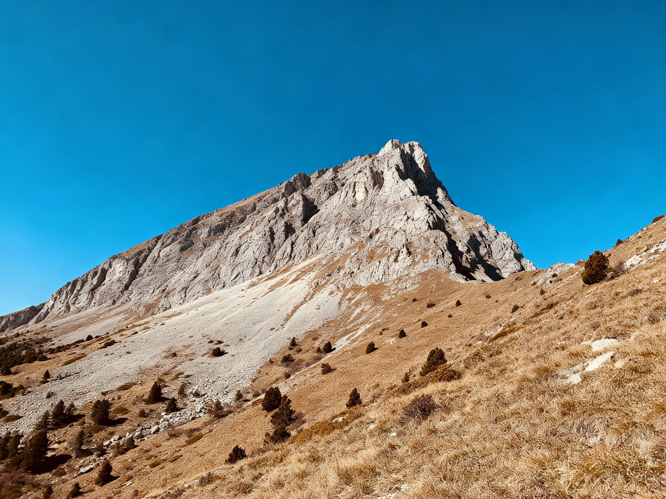 Towering gray rocky mountain peak with dry brown slopes and clear blue sky