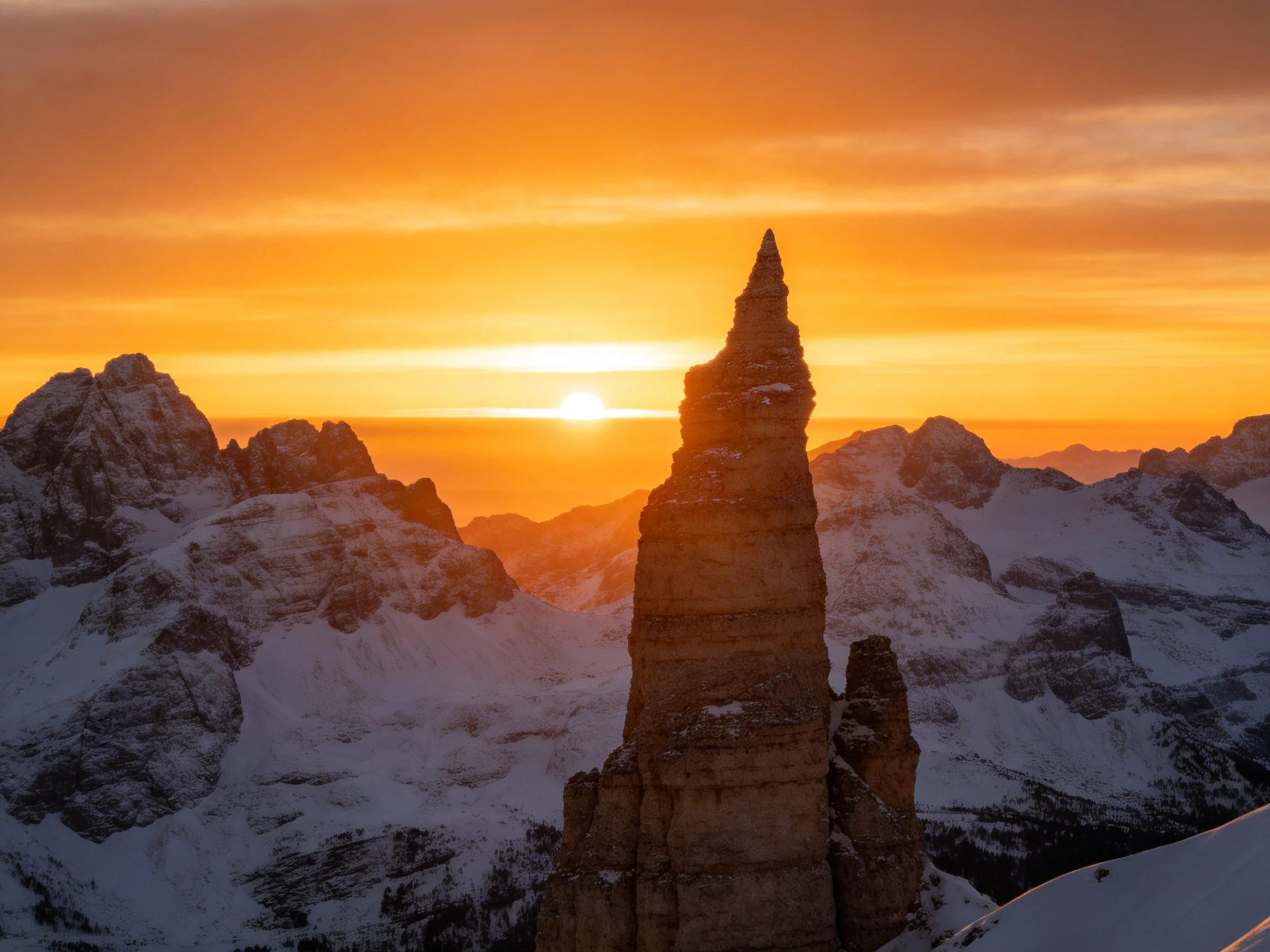 Towering rock formation amidst snow-capped mountains at sunset