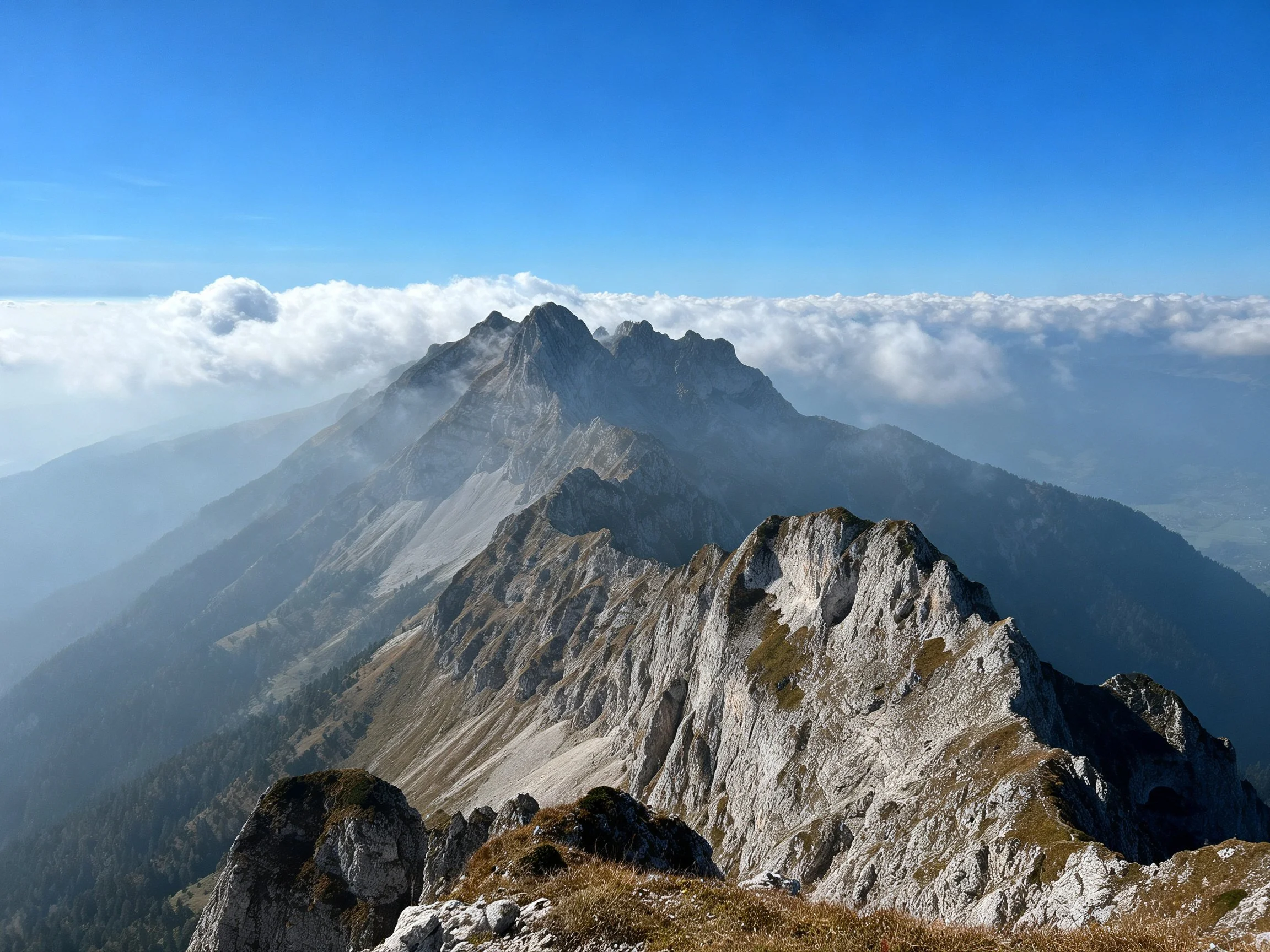 Towering rocky peaks rise above a sea of clouds under clear blue sky