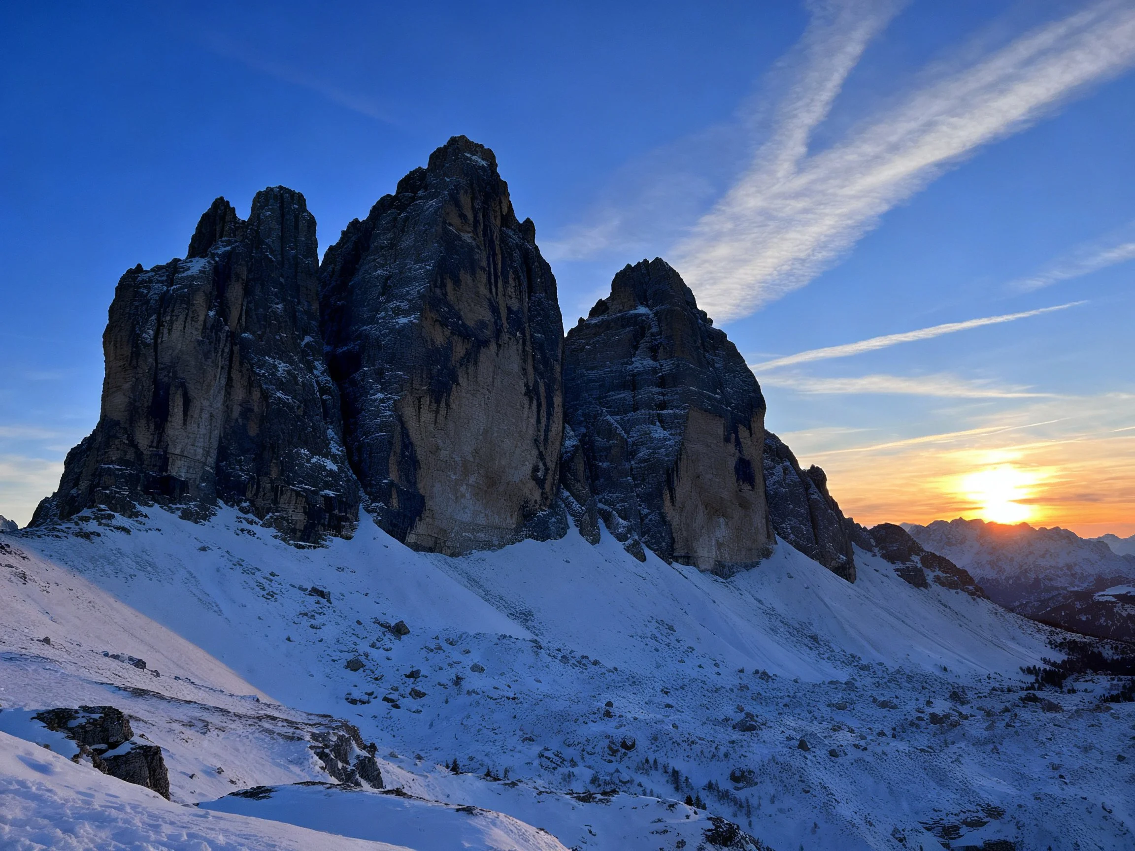 Towering rocky peaks with snow-covered slopes under a vibrant sunset sky