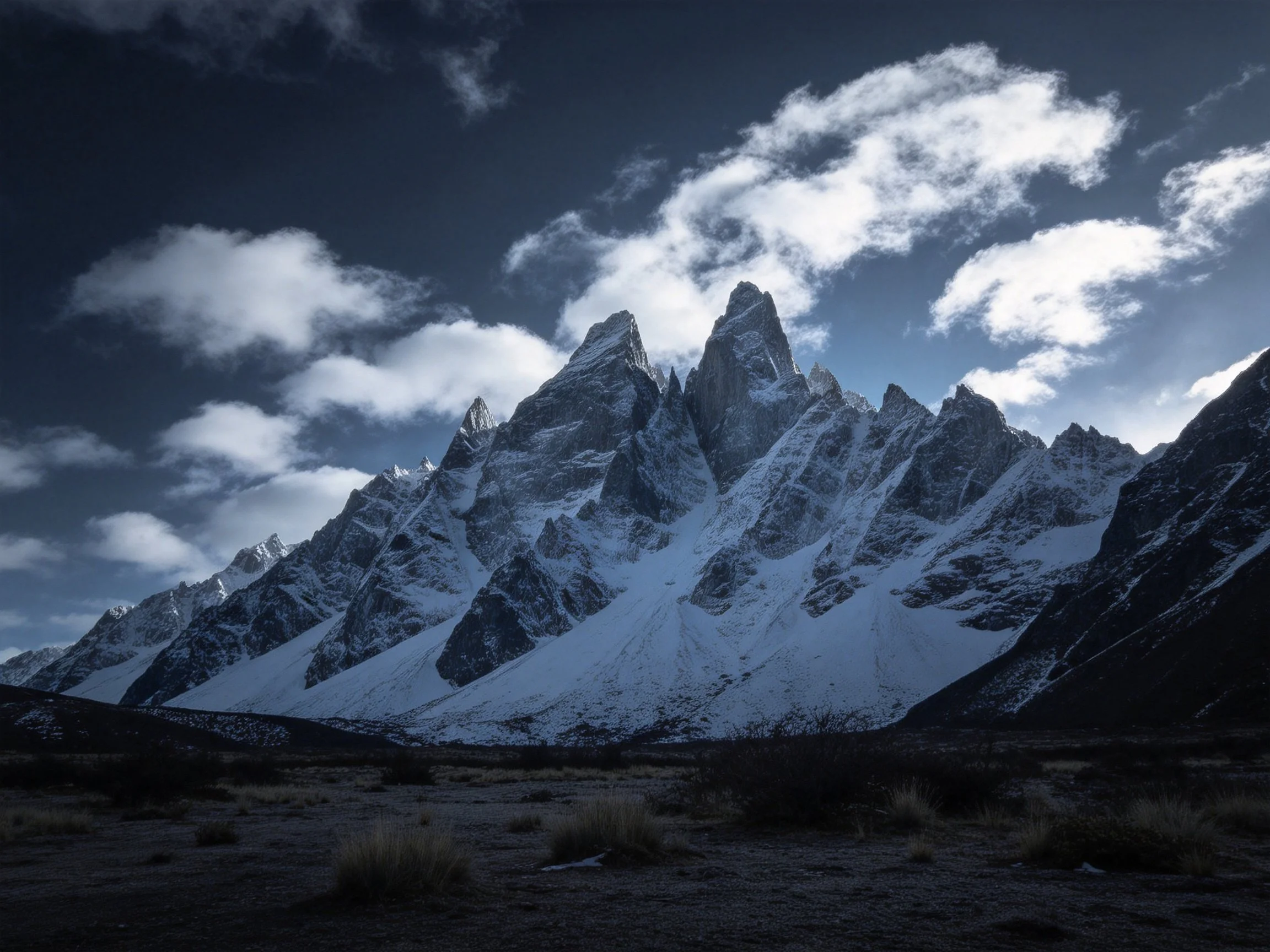 Towering snow - capped mountain peaks with dark rocky slopes under dramatic cloudy skies
