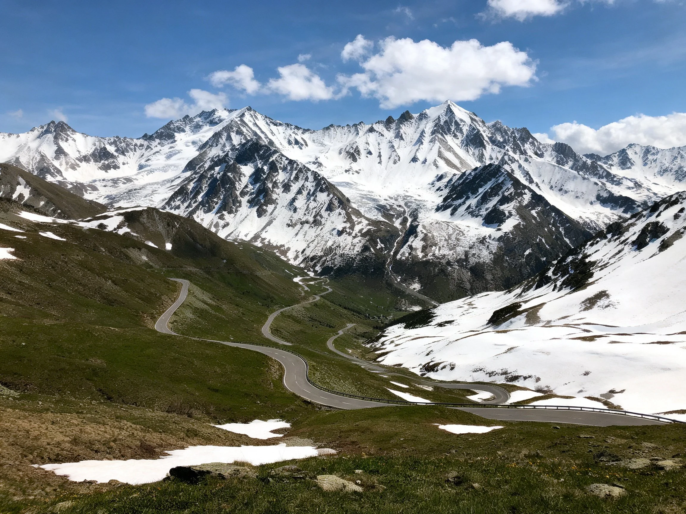 Towering snow - capped peaks with winding mountain roads and green slopes