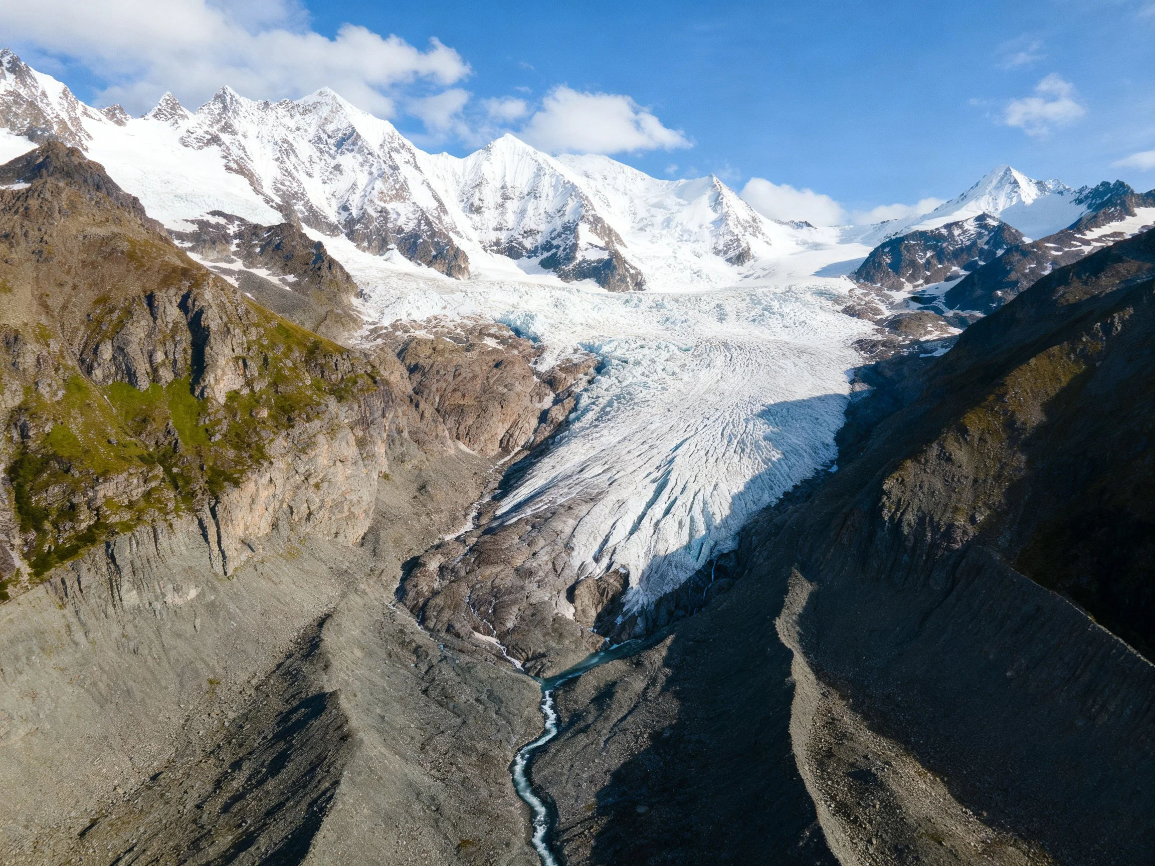 Towering snow - covered peaks encase a large glacier with rocky valleys