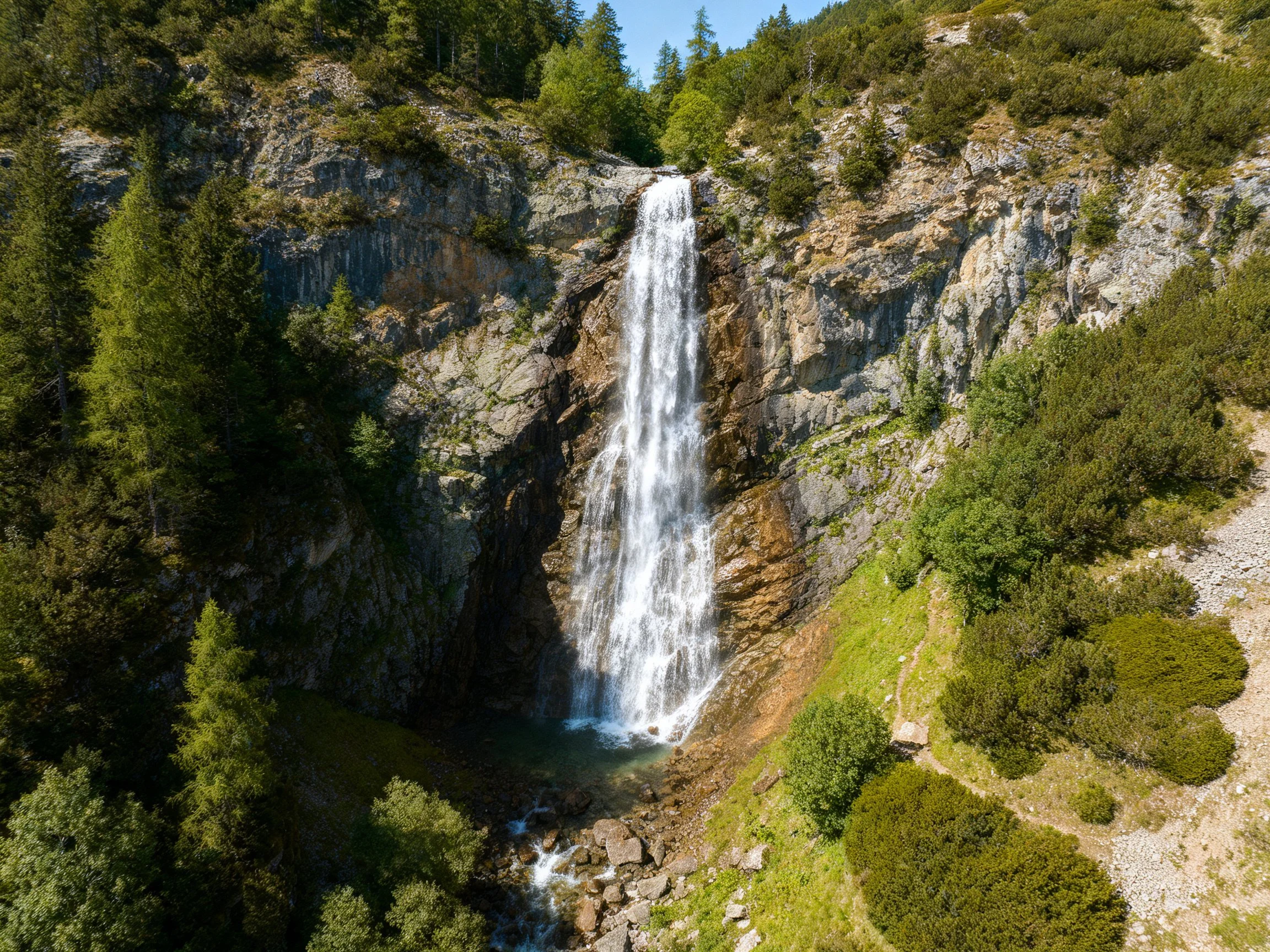 Towering waterfall flows over rugged cliff into lush forested landscape