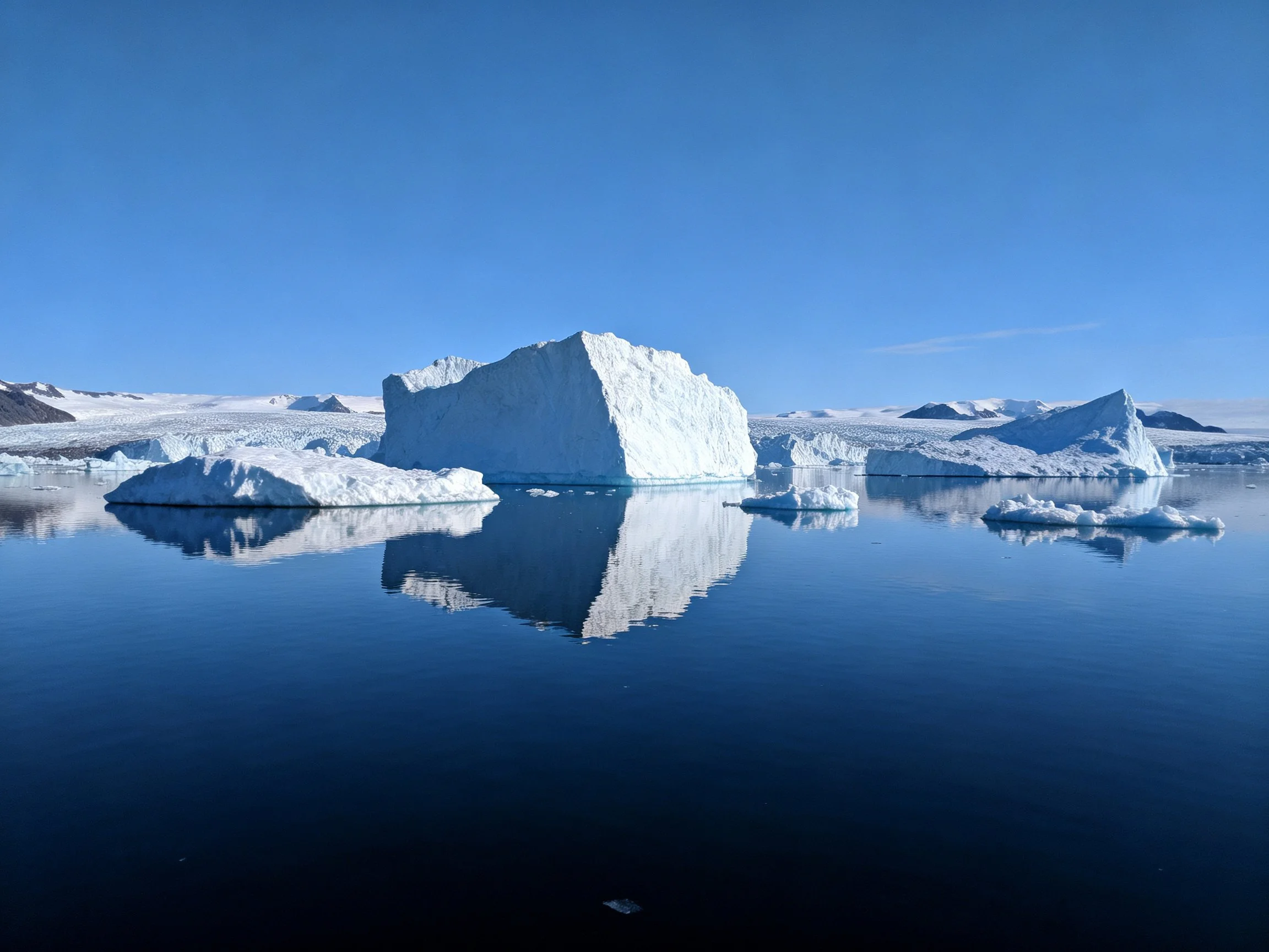Towering white iceberg, smaller icebergs, calm blue water, clear sky