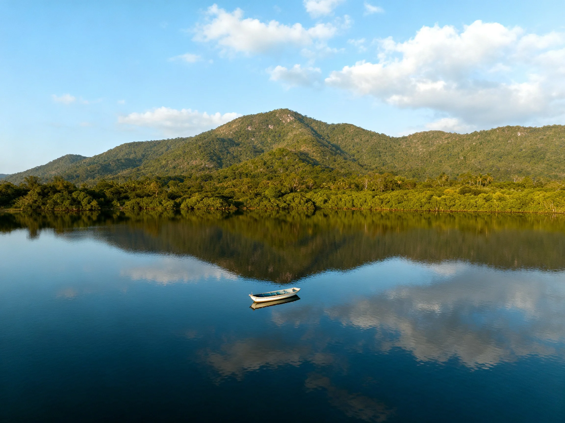 Tranquil lake reflects forested mountains under bright sky