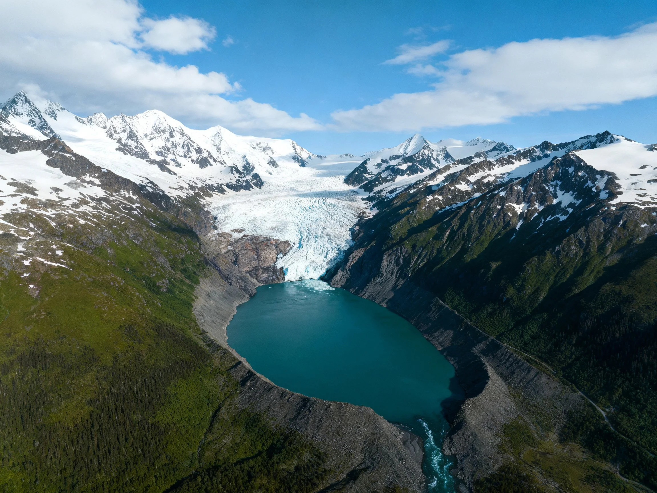 Turquoise Glacier Lake Between Snowy Peaks and Forested Slopes