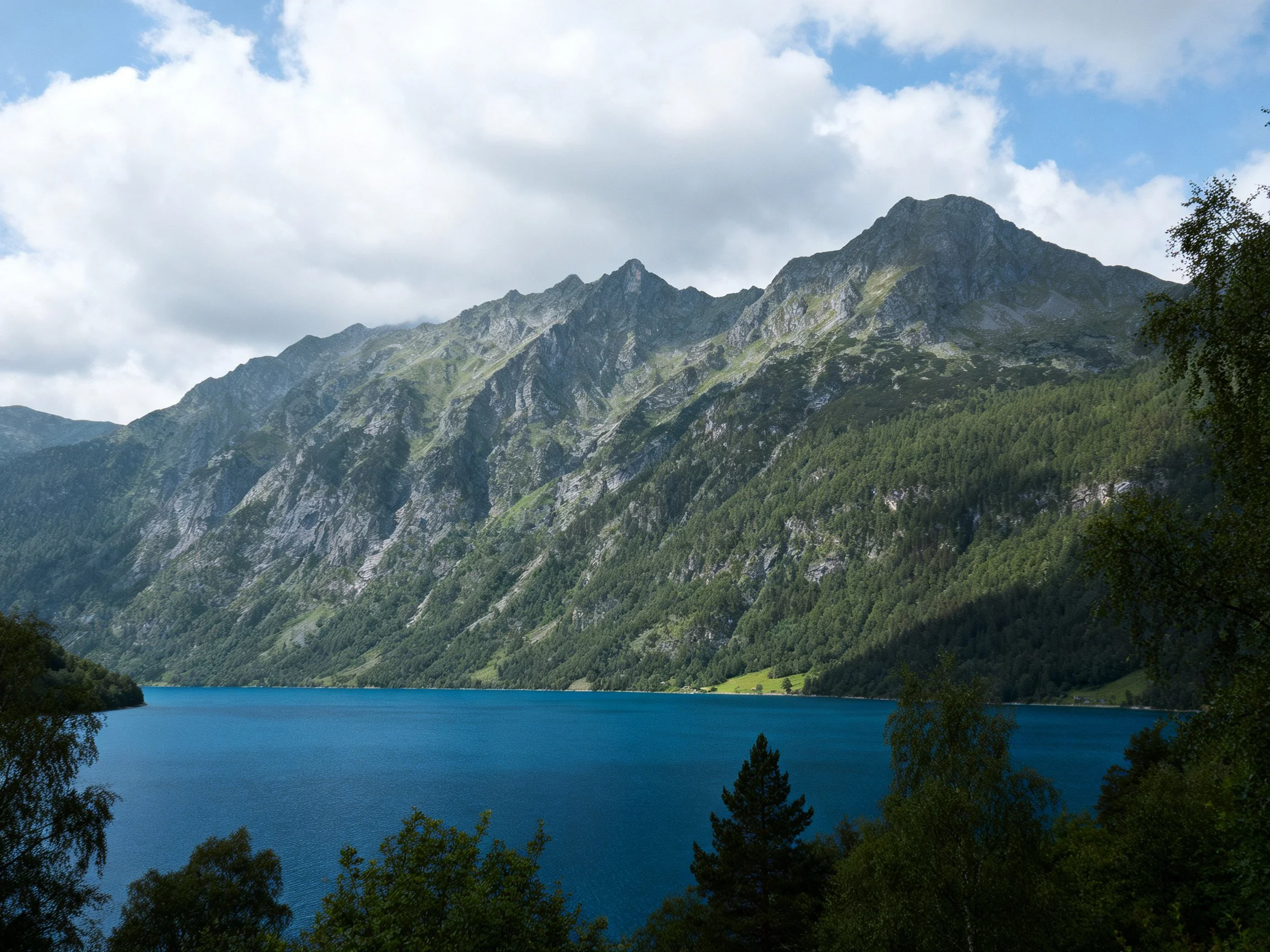 Turquoise lake framed by forested mountains under cloudy sky