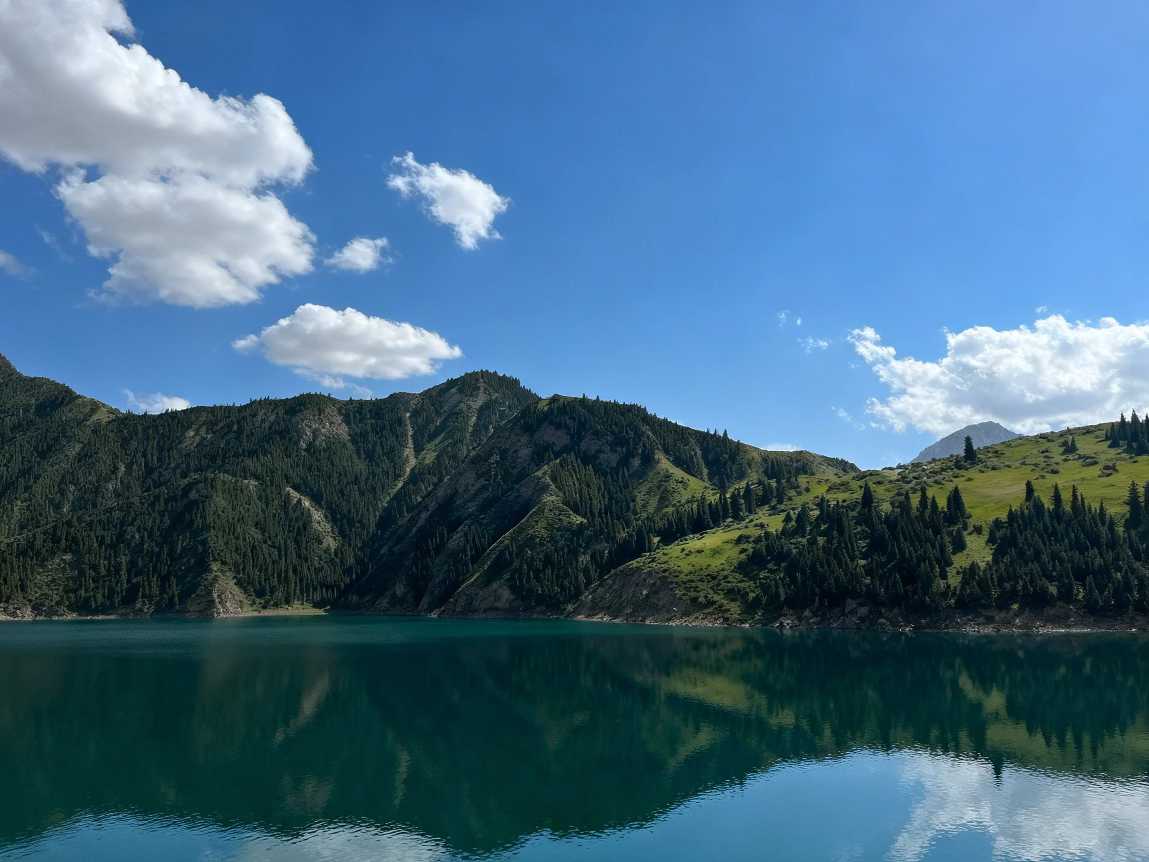 Turquoise lake reflects forested mountains under clear blue sky