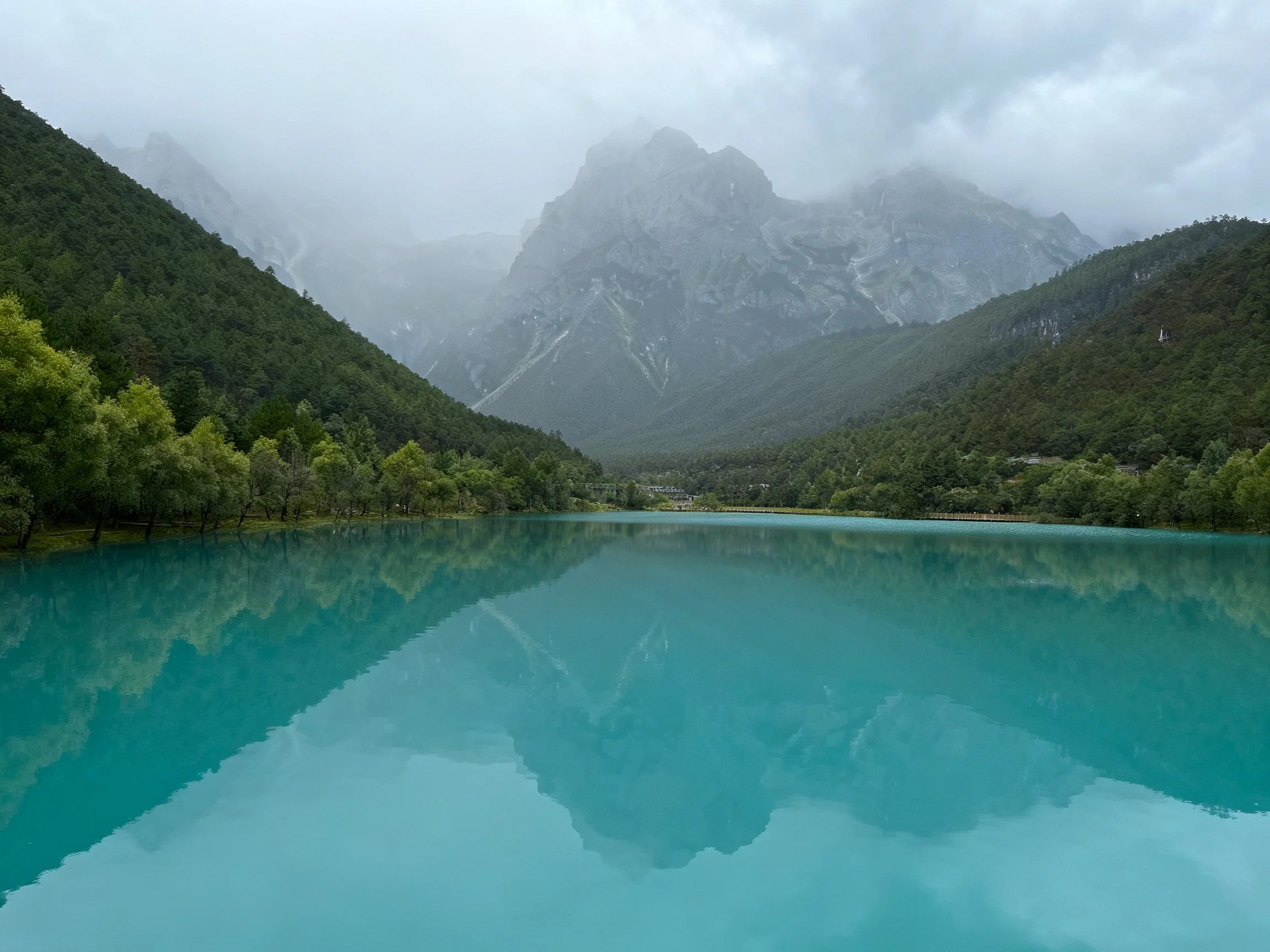Turquoise lake reflects misty mountains among lush forests