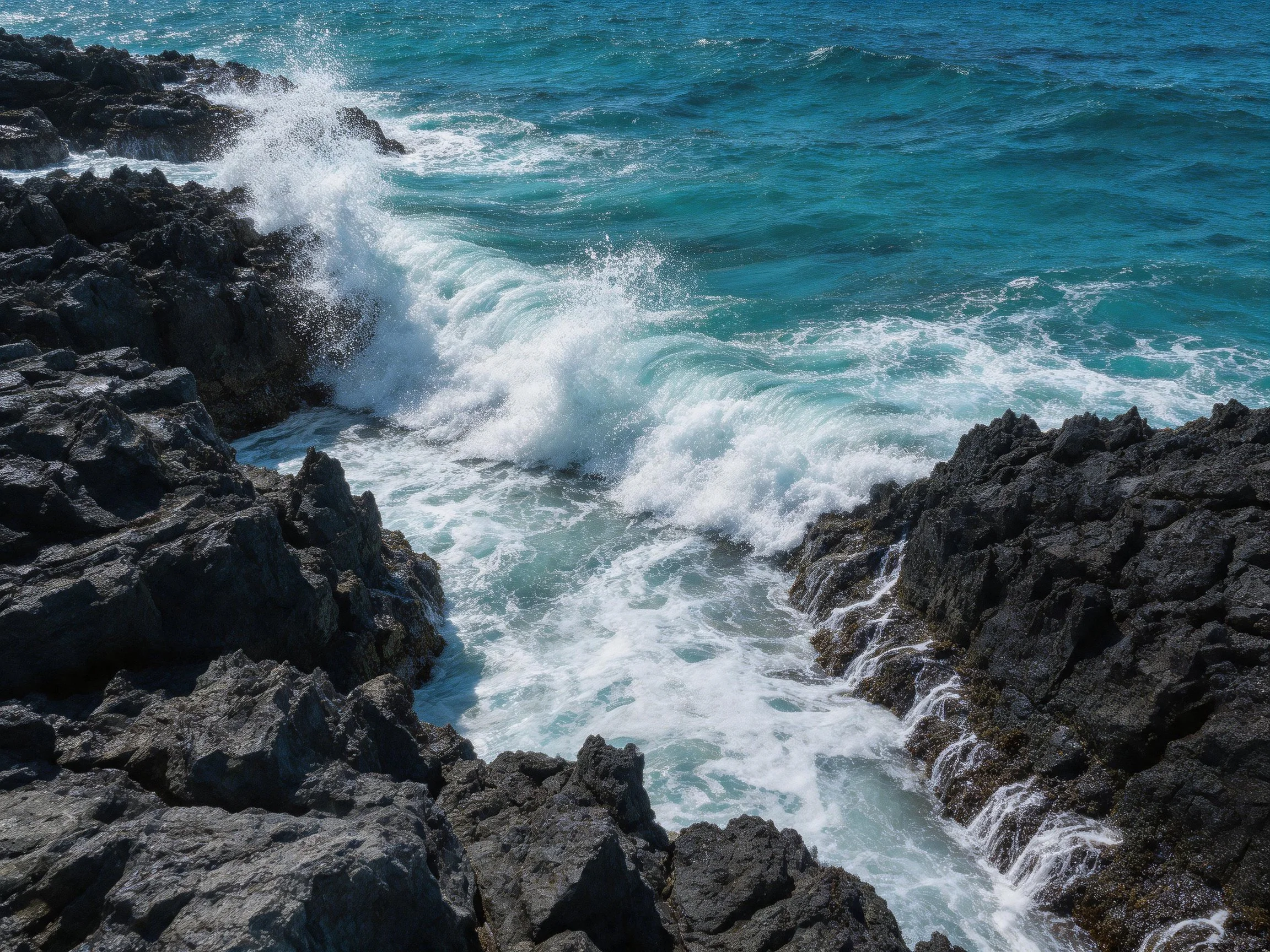 Turquoise ocean waves crash over rugged black rocks