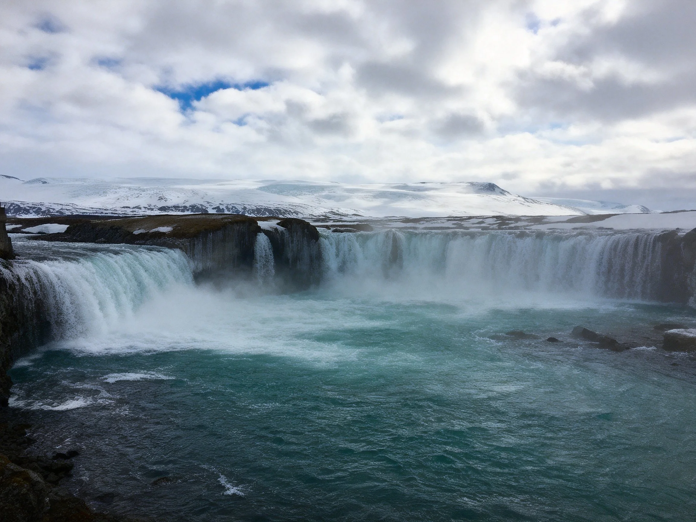 Turquoise waterfall cascades over dark rocky cliffs near snow-covered terrain