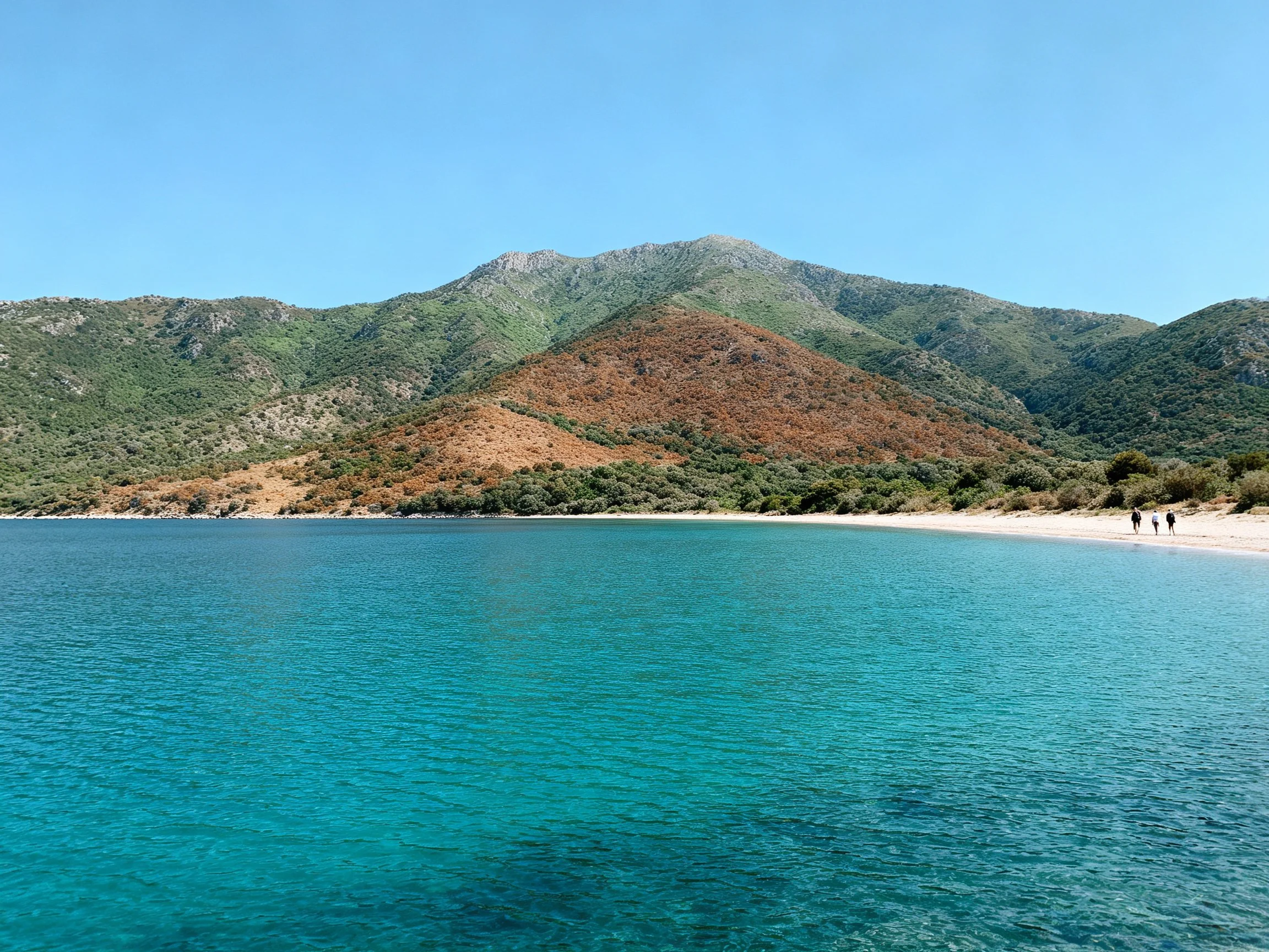 Turquoise waters border sandy beach with green-brown mountain backdrop