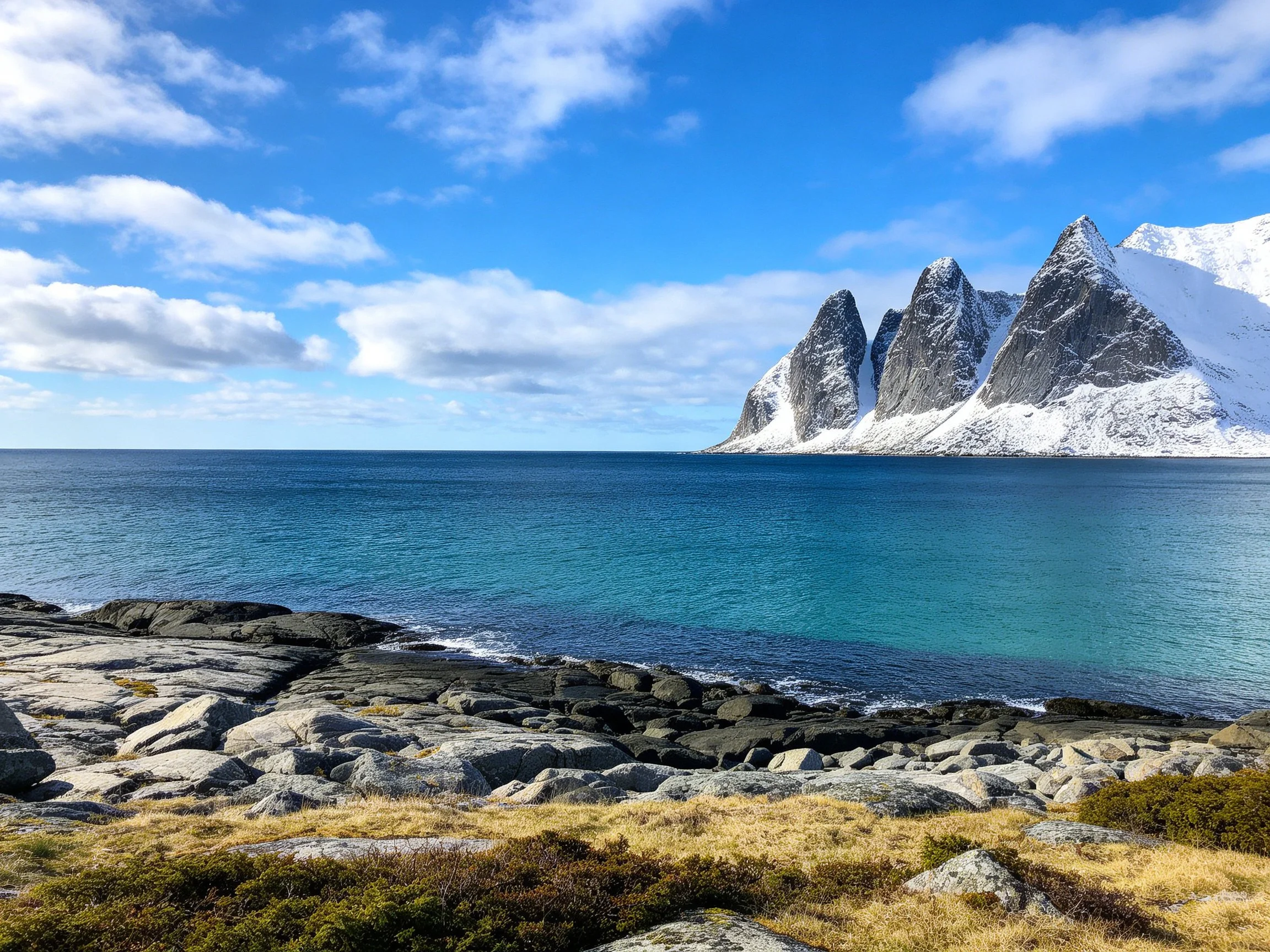 Turquoise waters meet rocky shores with snow-capped mountain backdrop