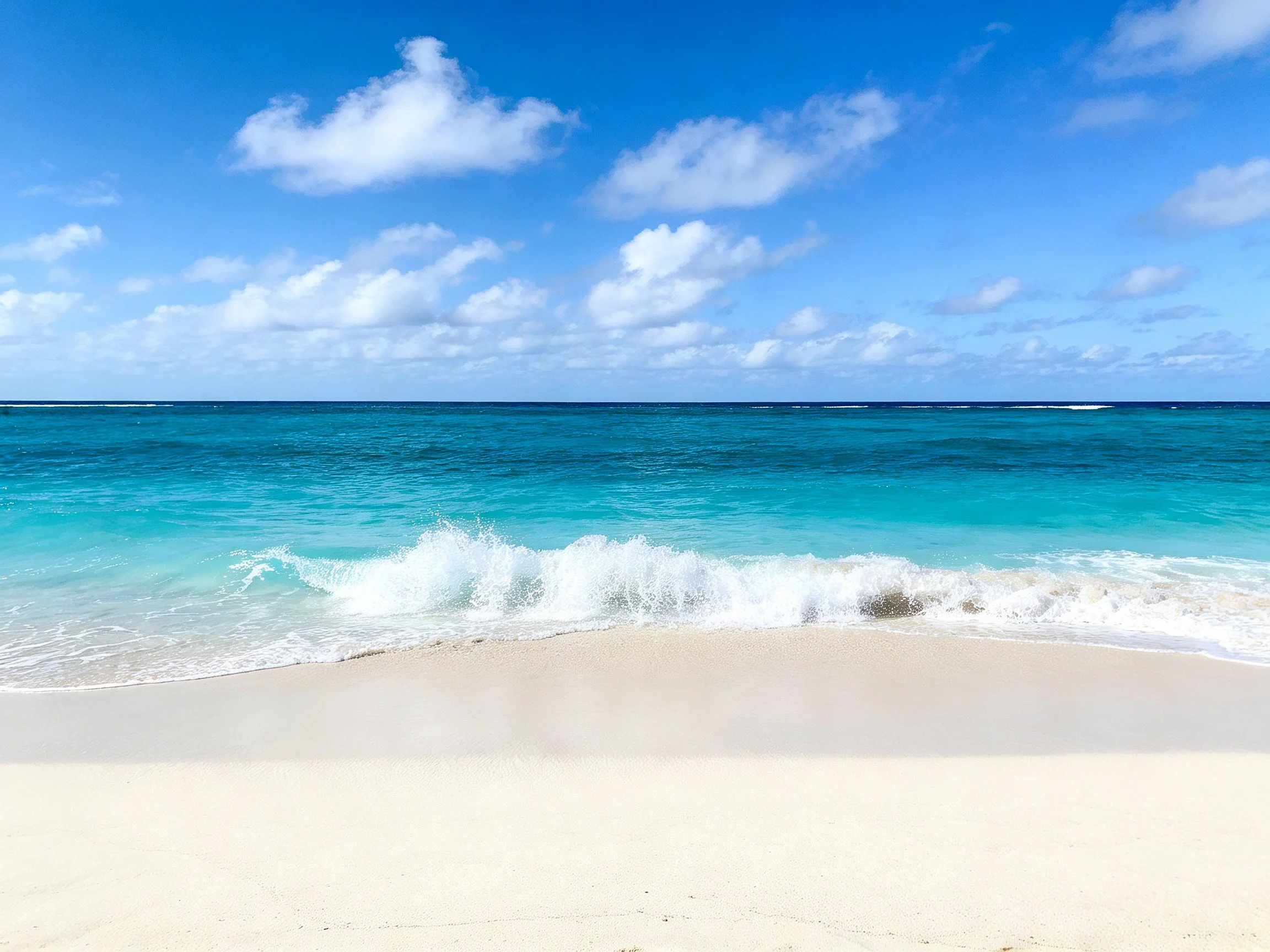 Turquoise waves crash onto pristine white sand under bright blue sky