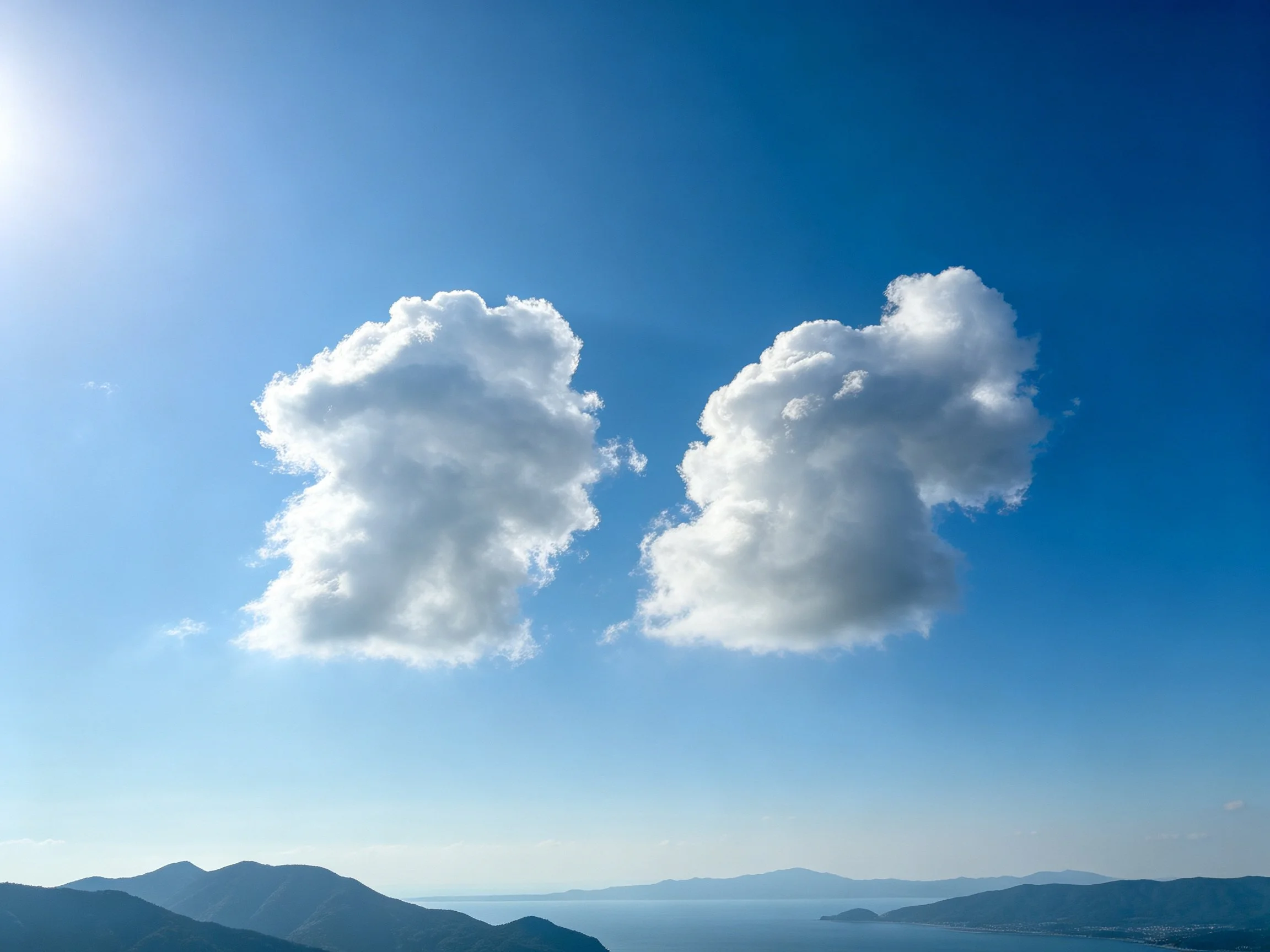 Two large white clouds float in a deep blue sky above mountain ranges