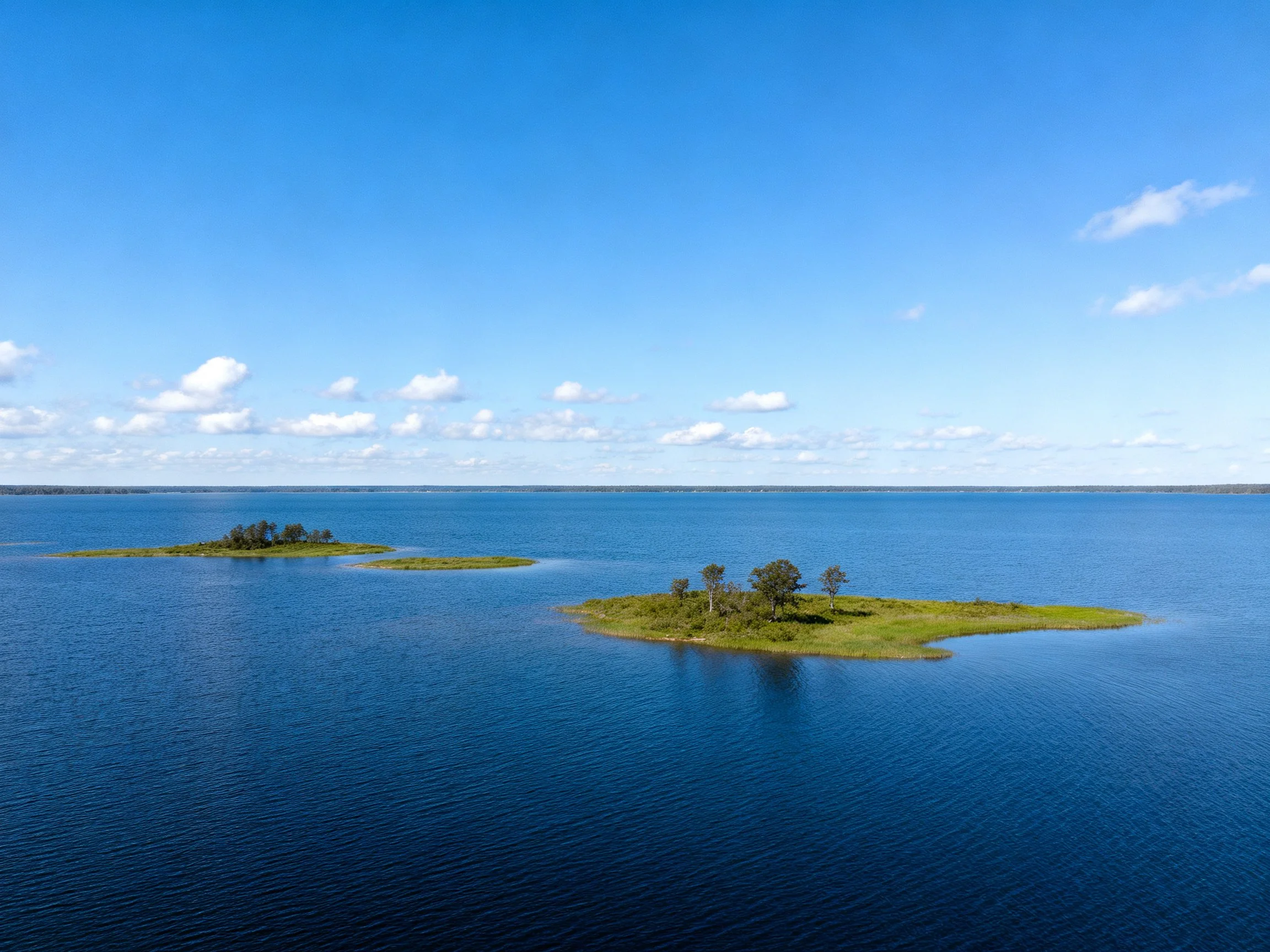 Two small green islands with trees in vast blue water under clear sky