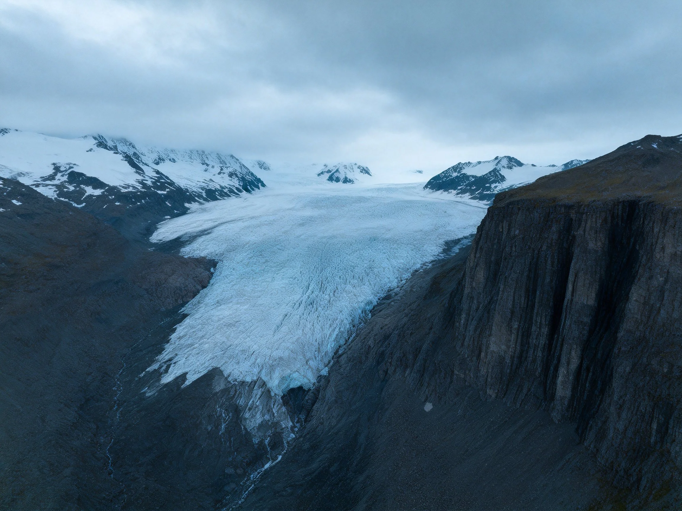 Vast glacier surrounded by snow - capped mountains and dark rocky cliffs