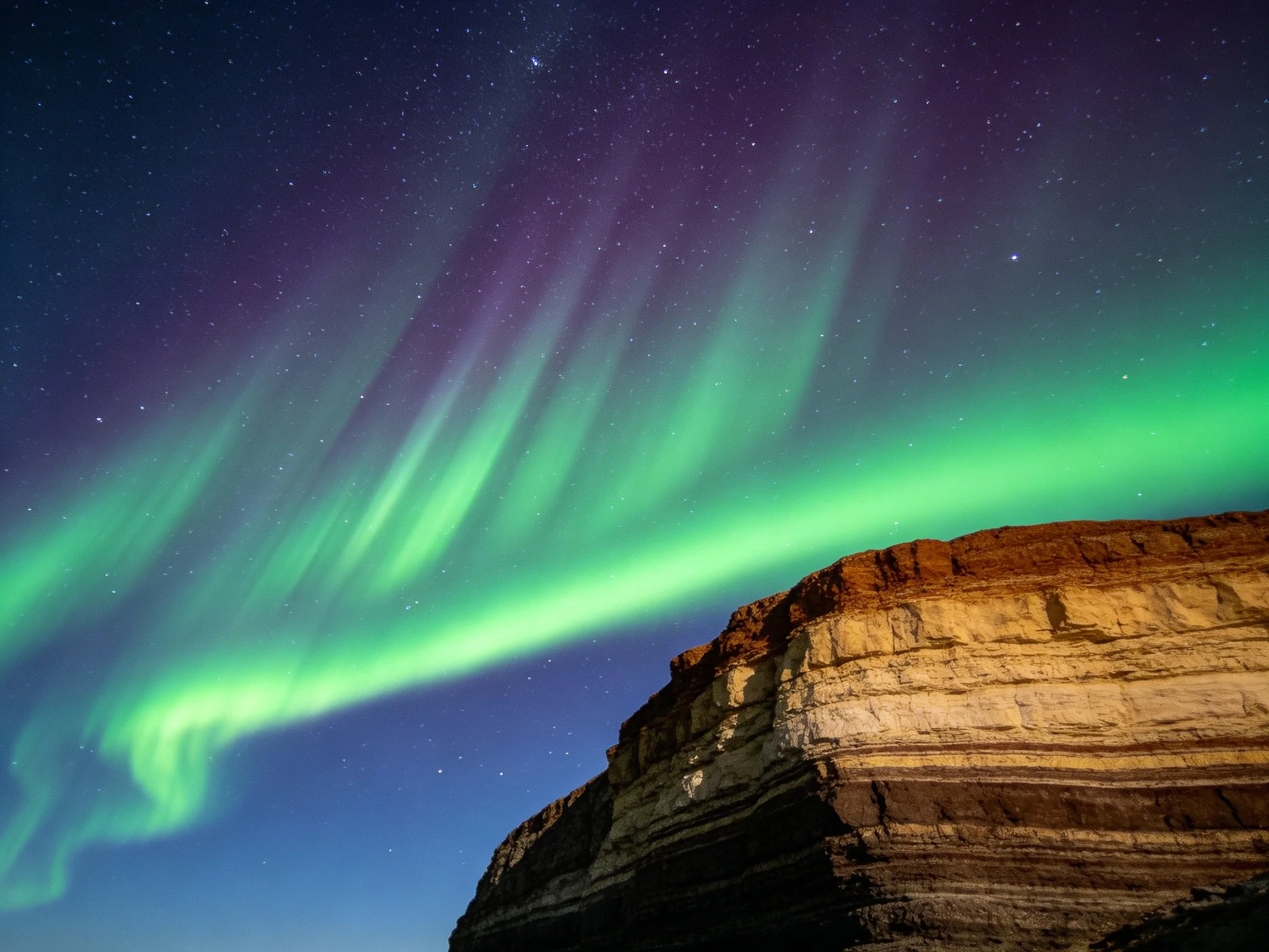 Vibrant aurora borealis illuminates layered rocky cliffs at night