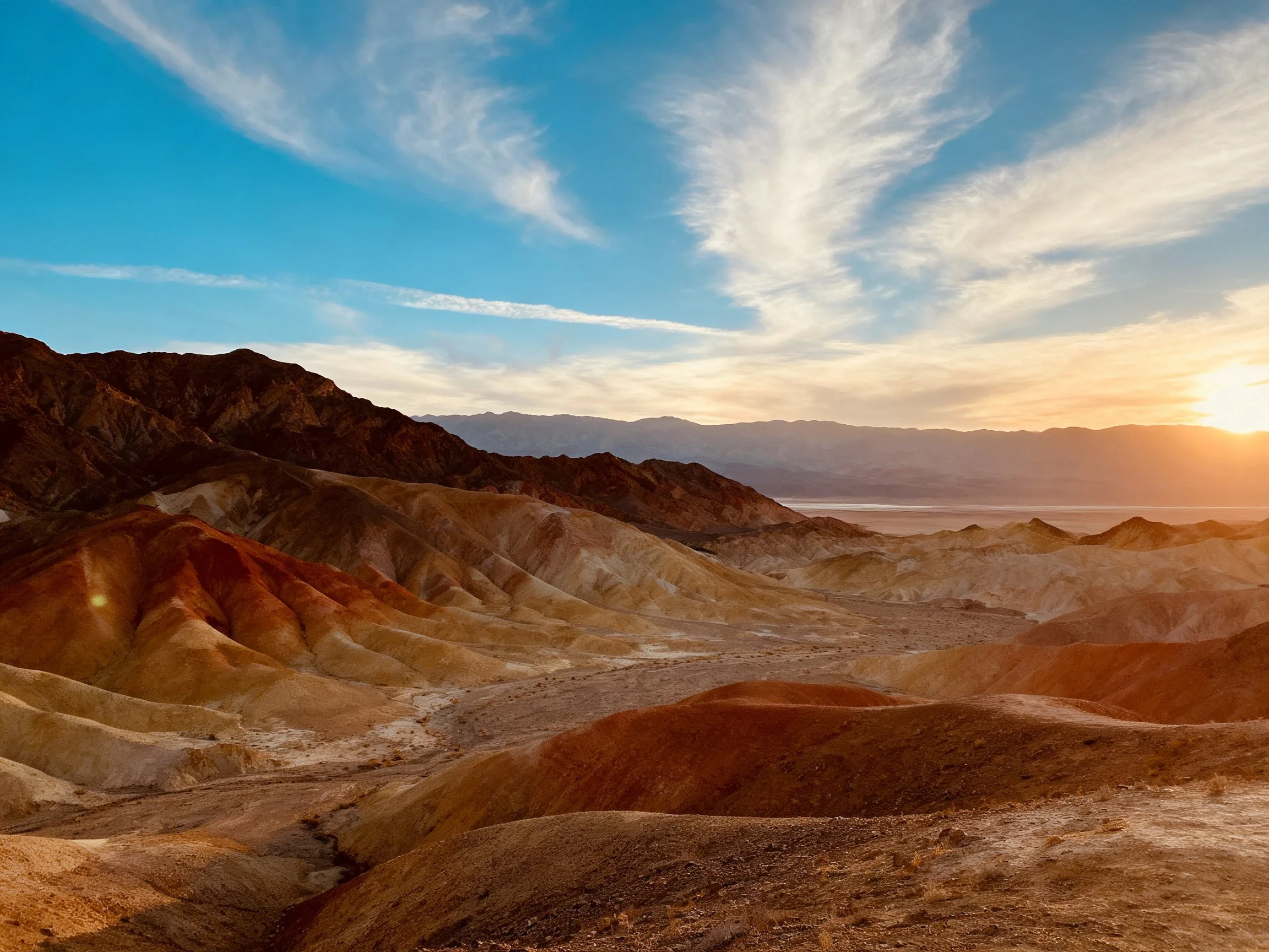 Vibrant multicolored desert hills under a sunset sky with distant mountains