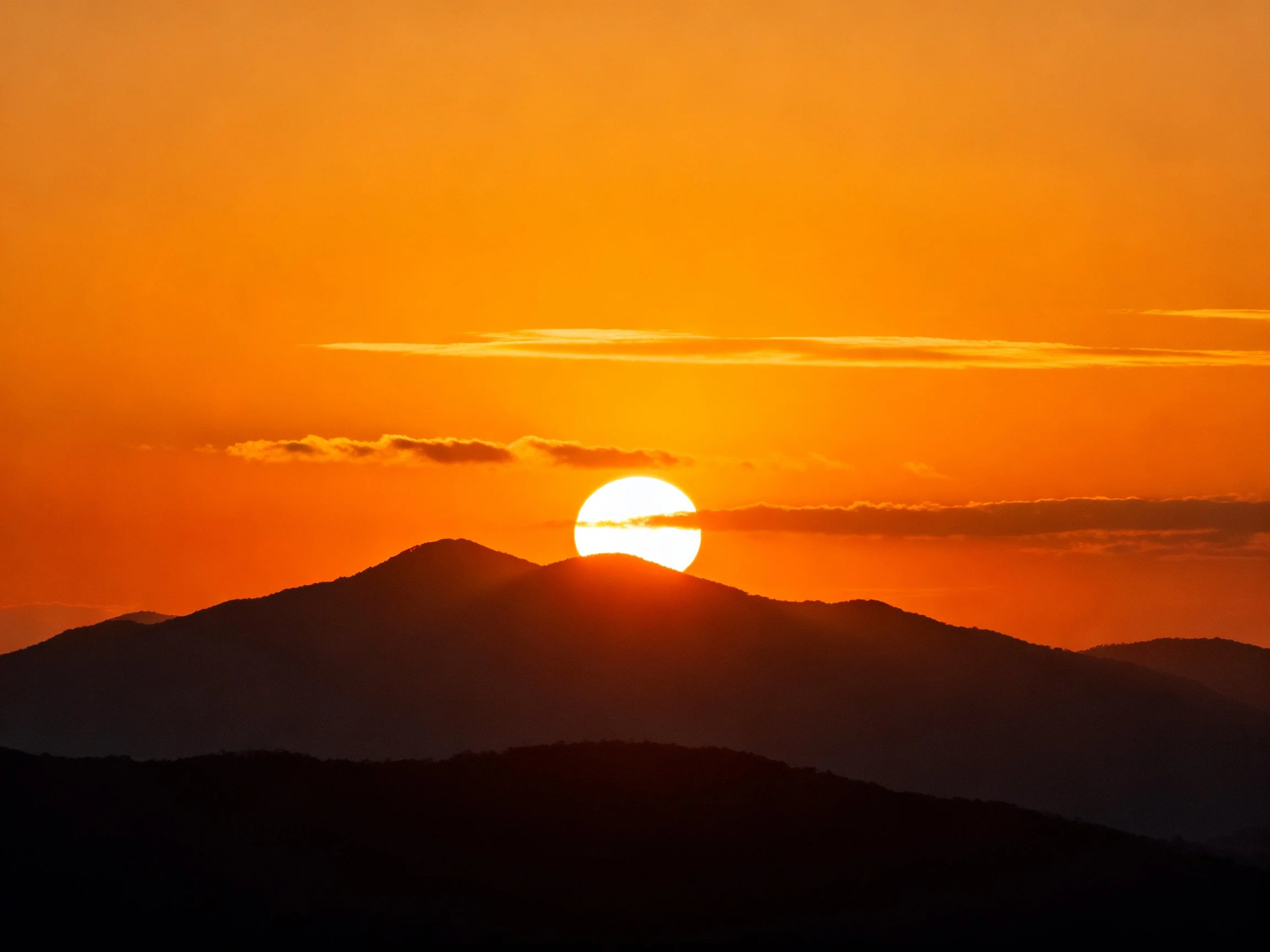 Vibrant orange sunset behind layered mountain silhouettes