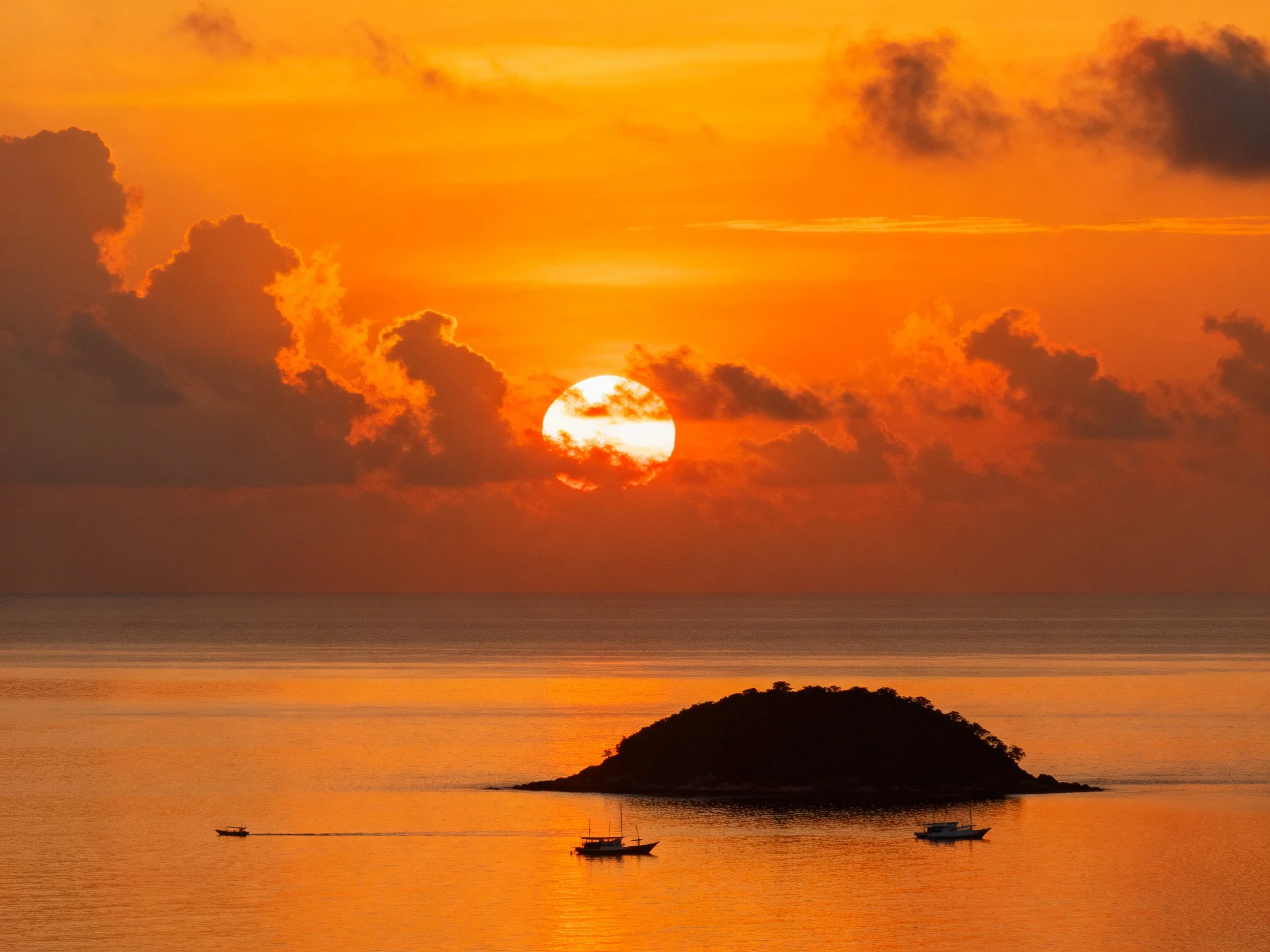 Vibrant orange sunset over calm sea with small island and boats