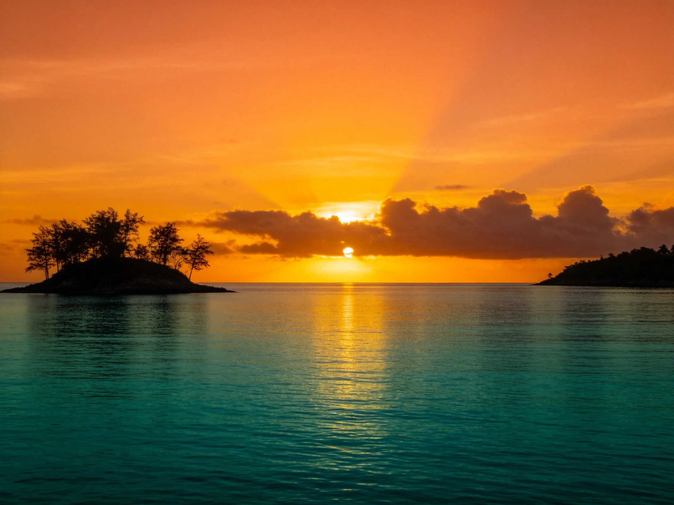 Vibrant orange sunset over turquoise waters near two tree-covered islands