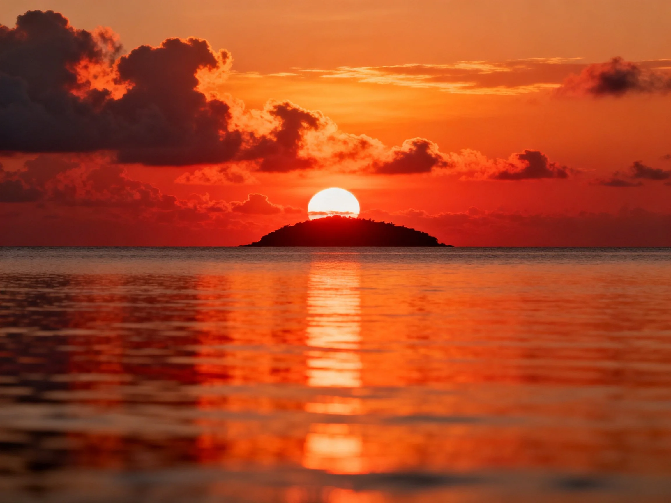Vibrant orange sunset reflects over calm waters near small island