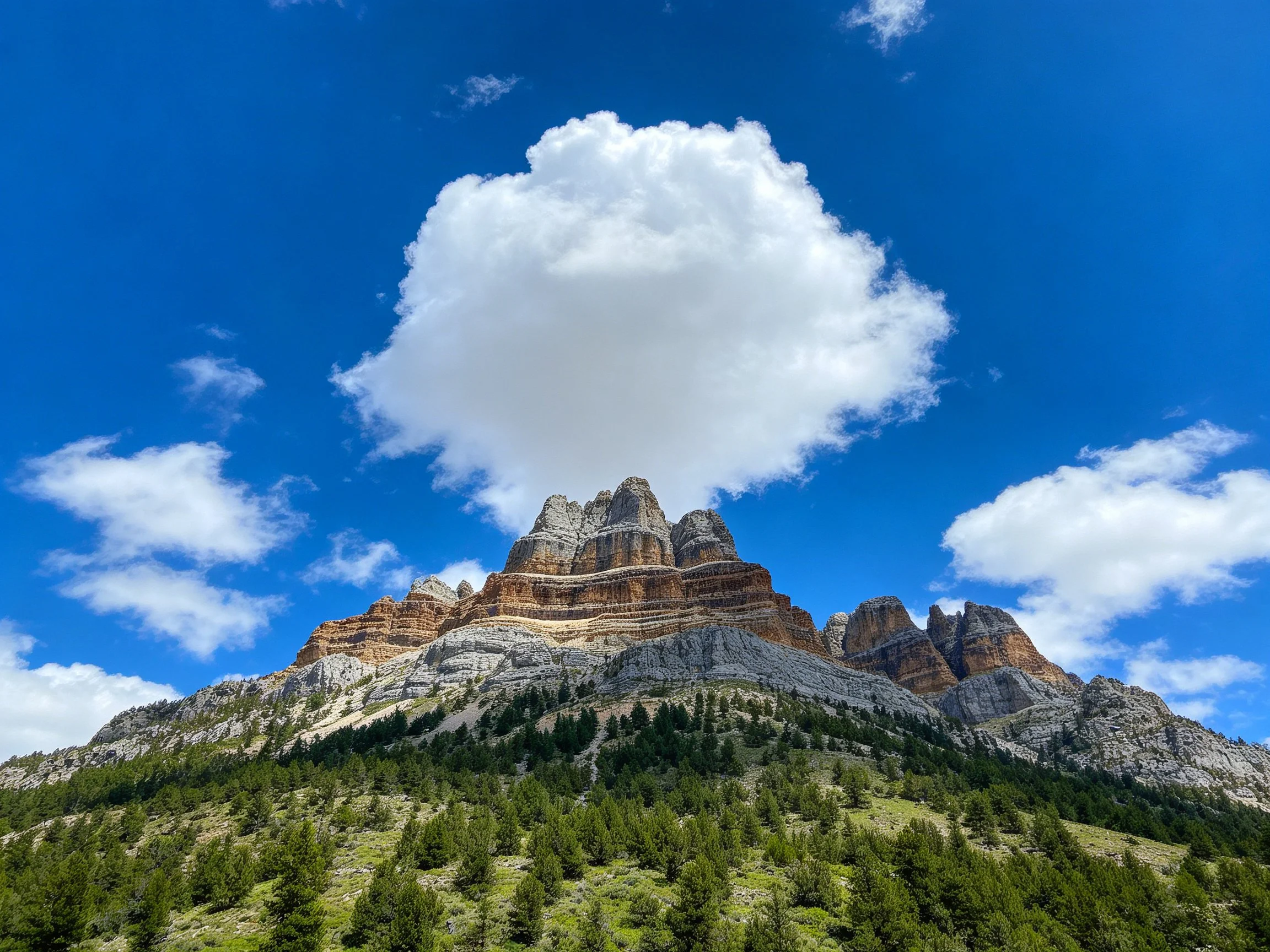 Vibrant rocky mountain peak under bright blue sky with fluffy cloud