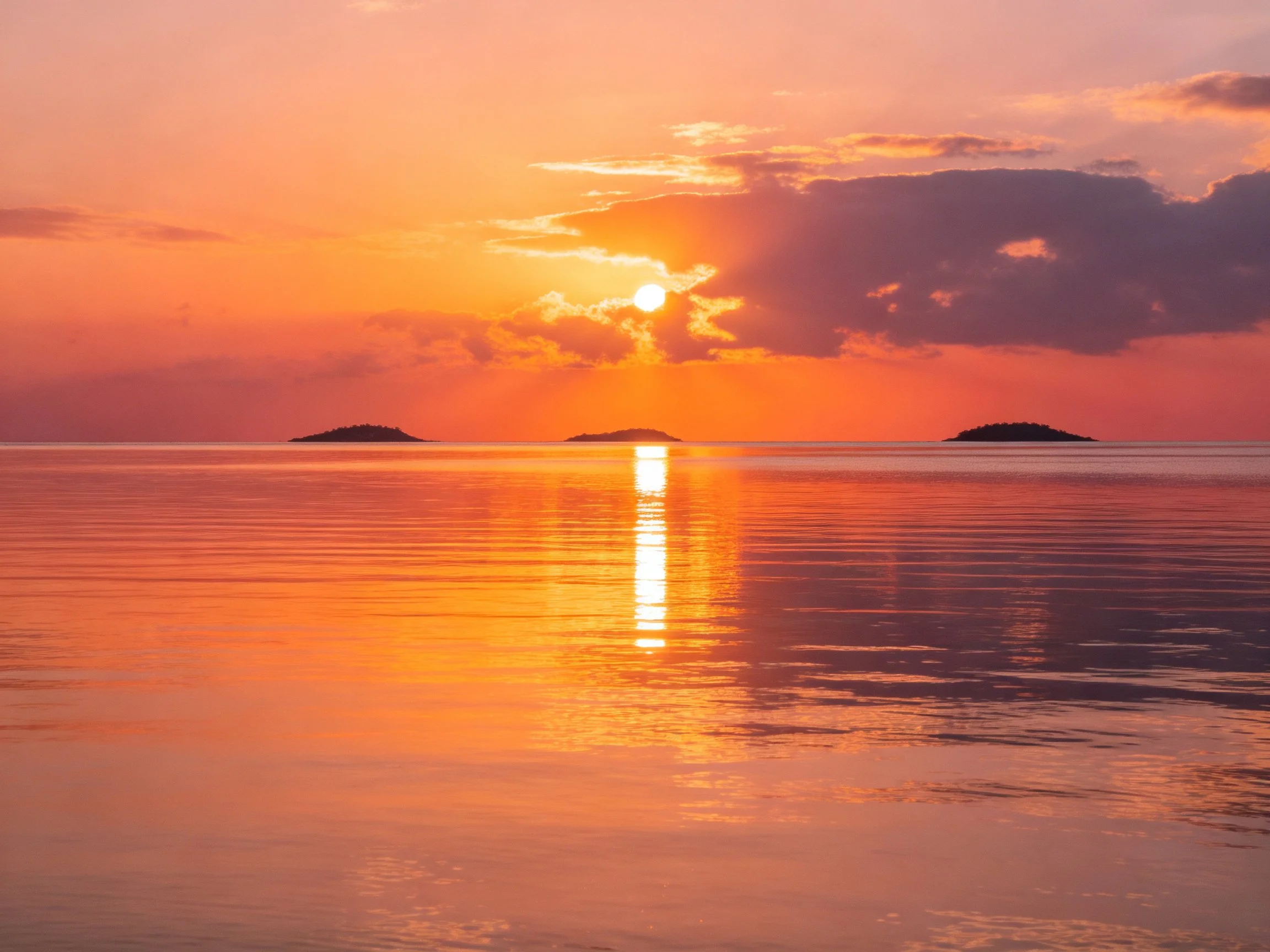 Warm-hued sunset reflects on calm sea near small islands