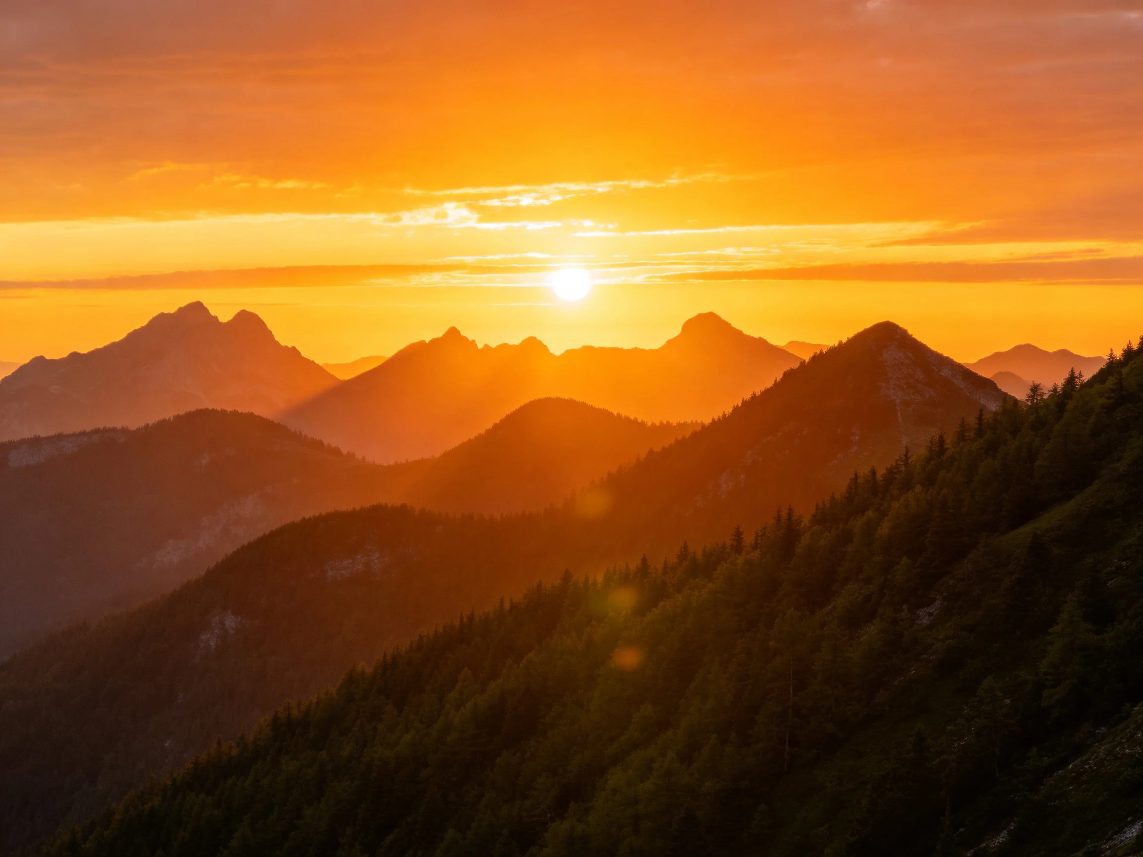 Warm orange sunset over layered mountain landscapes