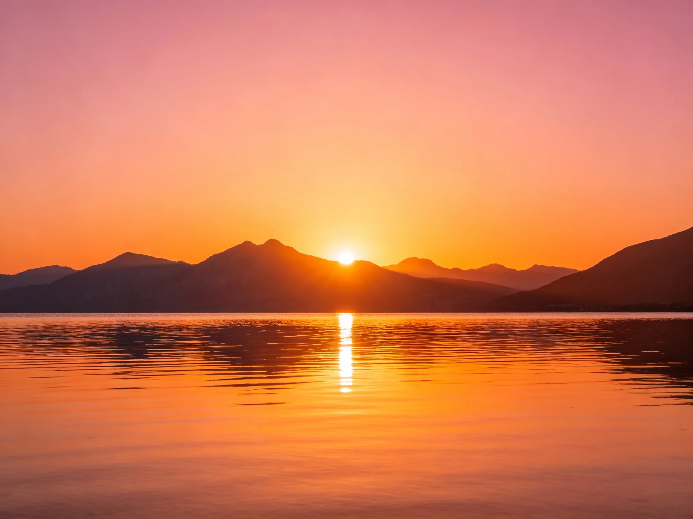 Warm orange sunset over mountain range reflecting in calm water