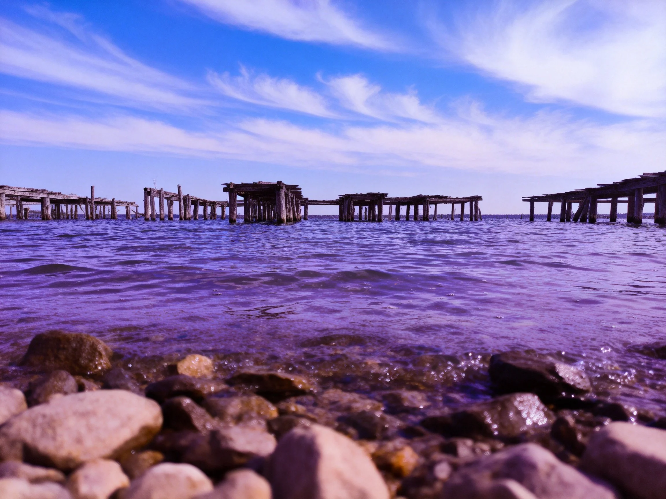 Weathered Wooden Piers Over Purple-Hued Water with Rocky Shoreline