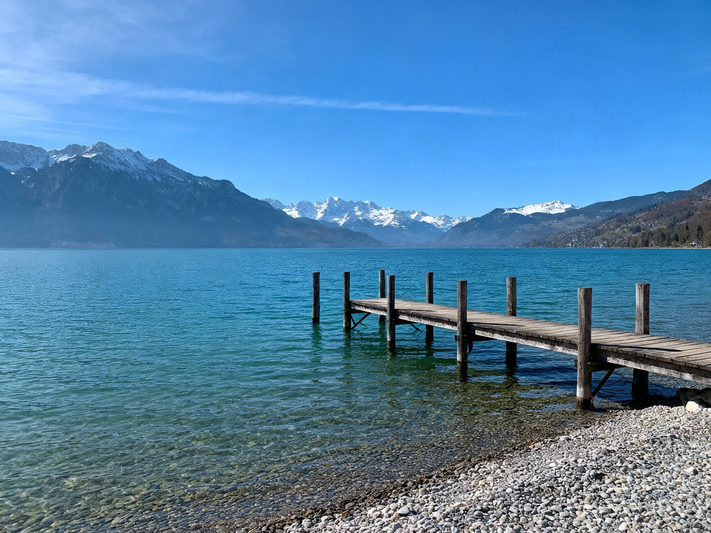 Weathered wooden dock extends into turquoise lake near snow-capped mountains