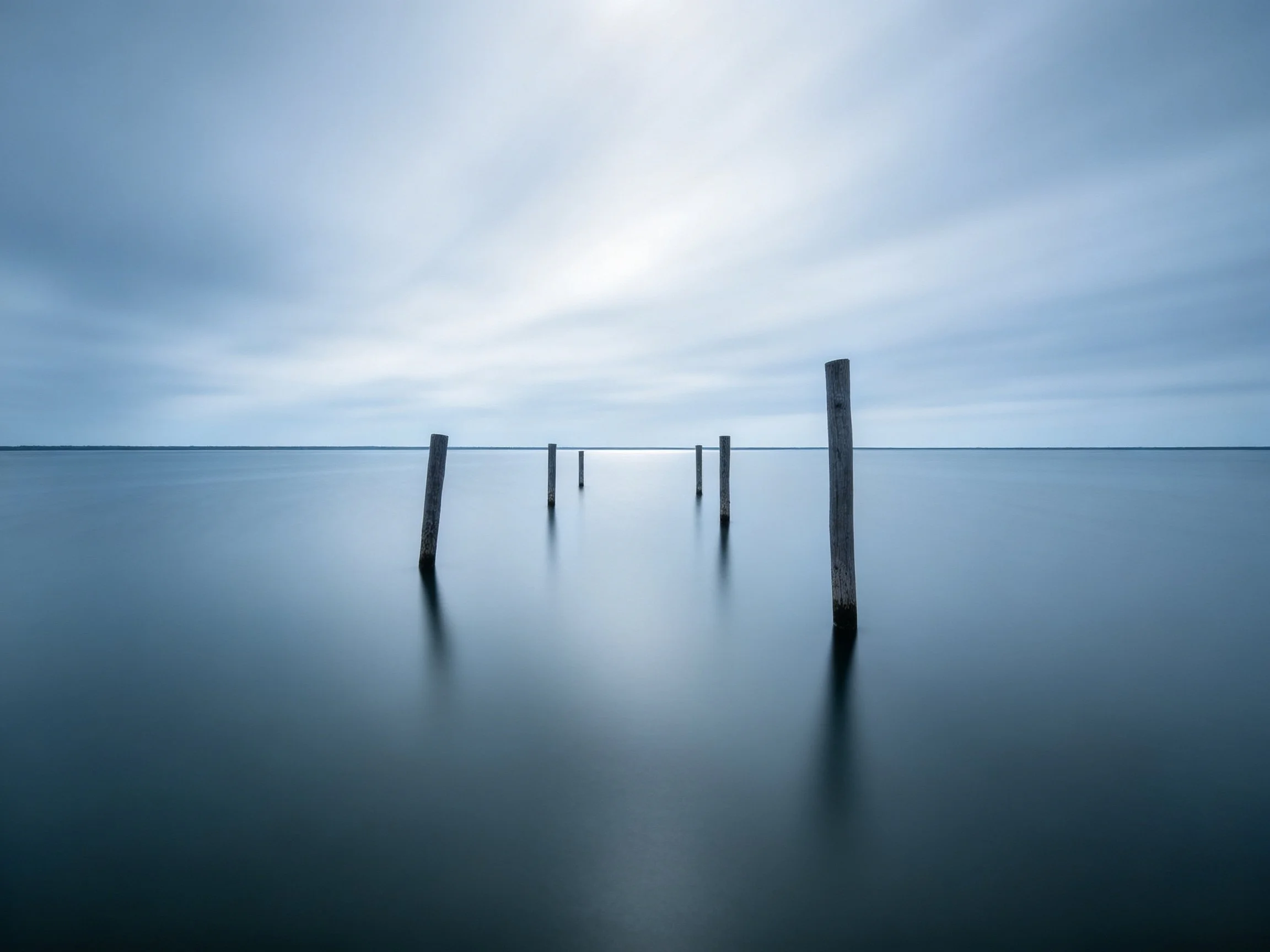 Weathered wooden posts in calm blue waters under overcast sky