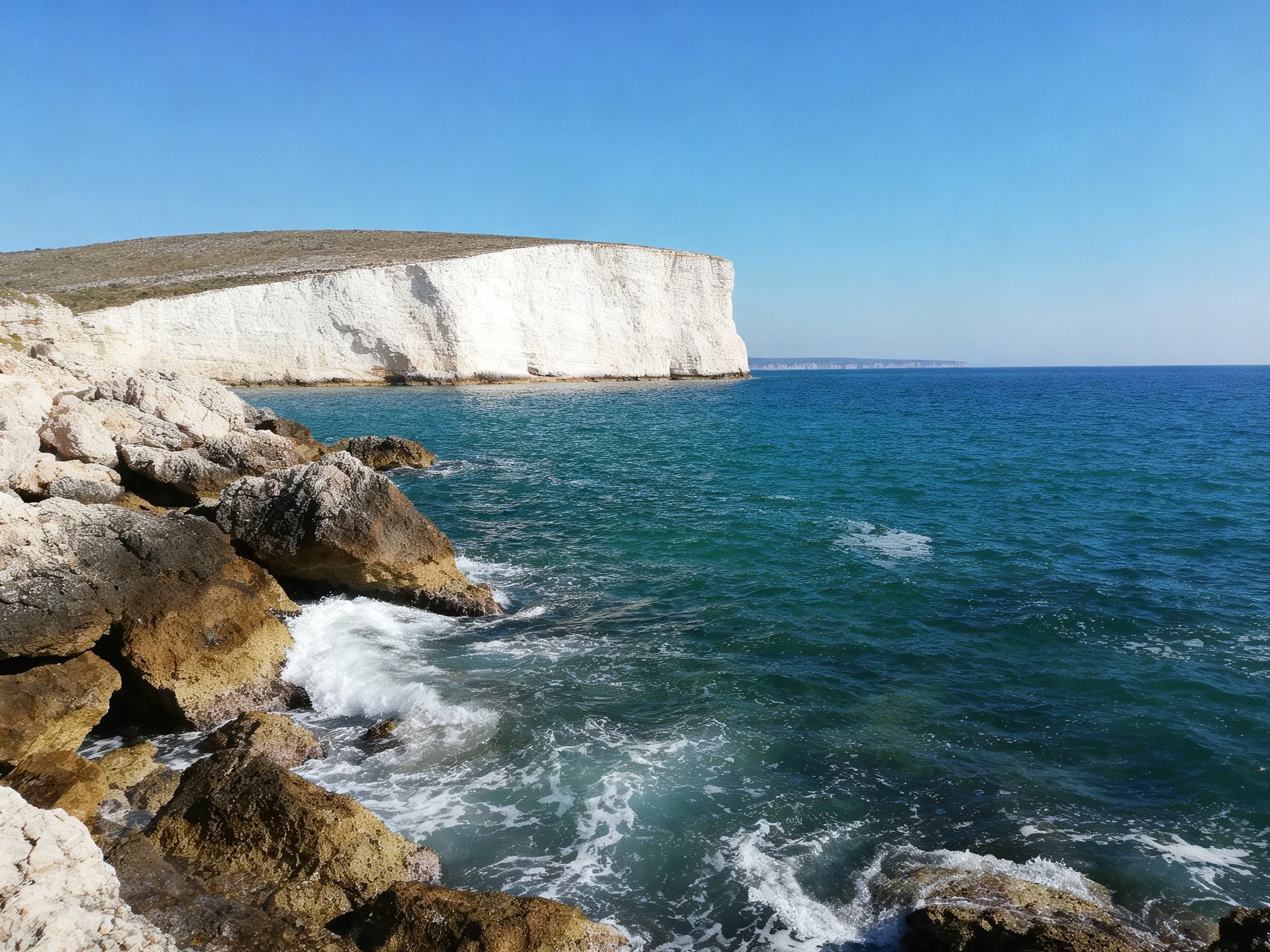 White chalk cliffs border turquoise ocean near rocky shore