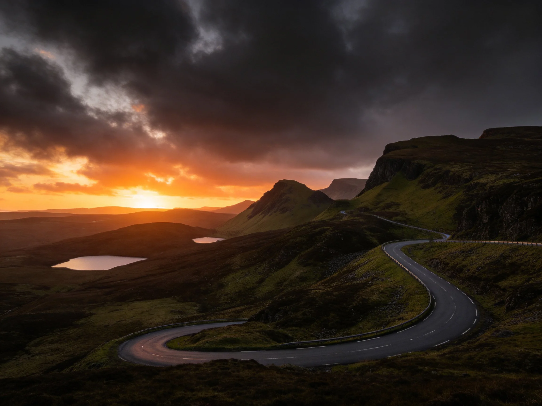 Winding mountain road under dramatic sunset with dark clouds