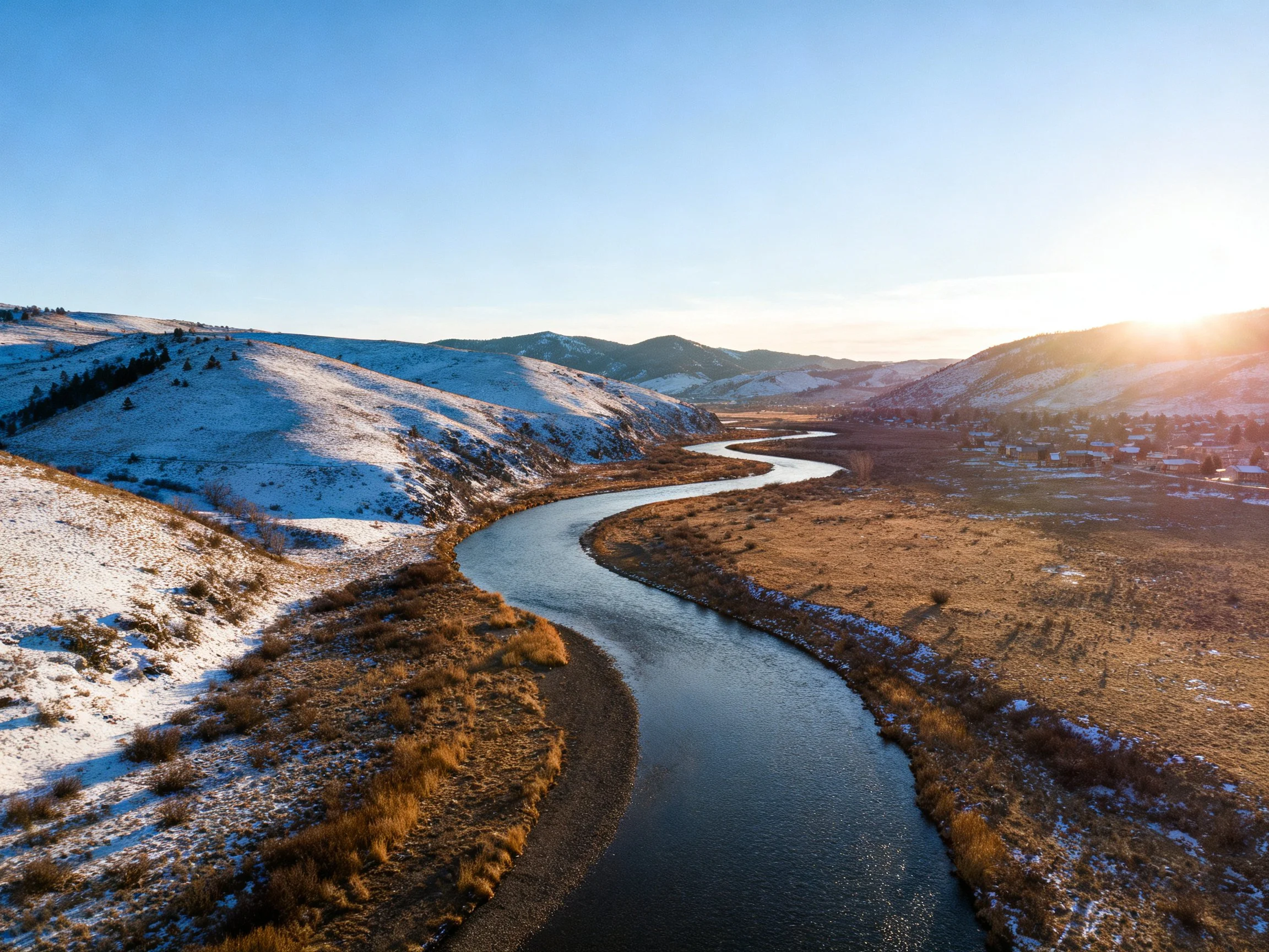 Winding river flows through snow-dusted hills and golden plains