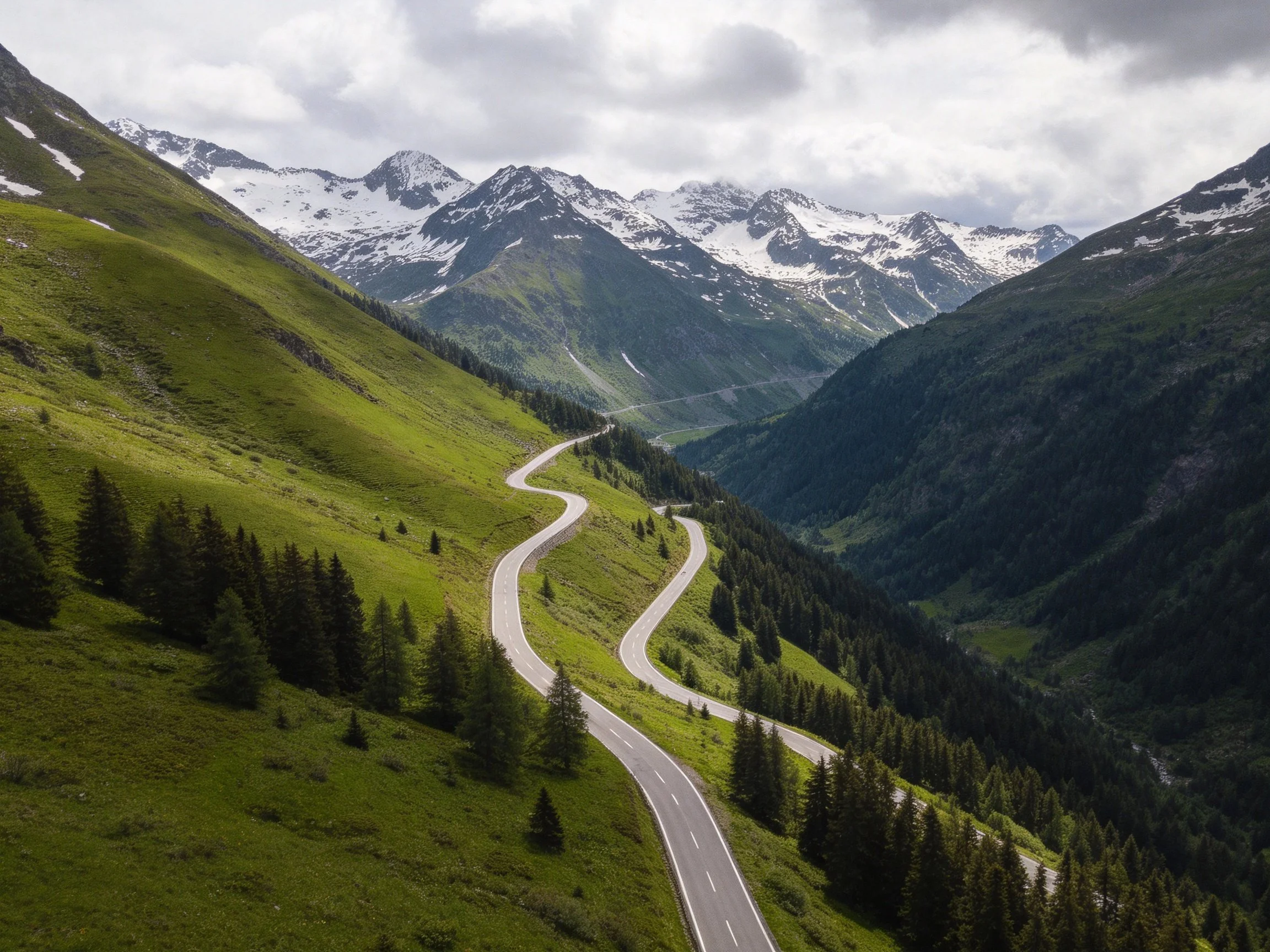 Winding road through lush green hills toward snow - capped mountains