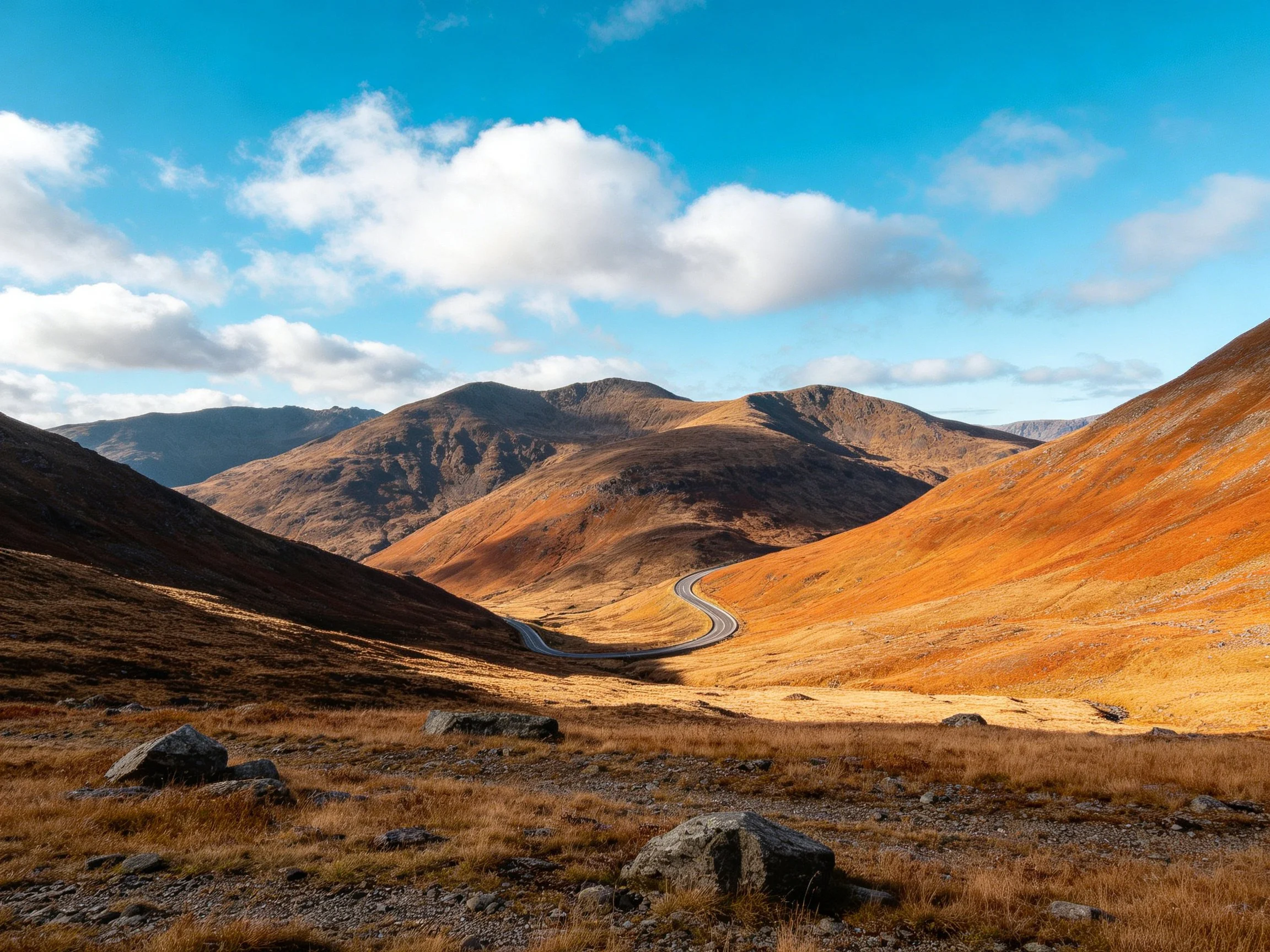 Winding road through vibrant autumn-colored mountain slopes under a clear blue sky.