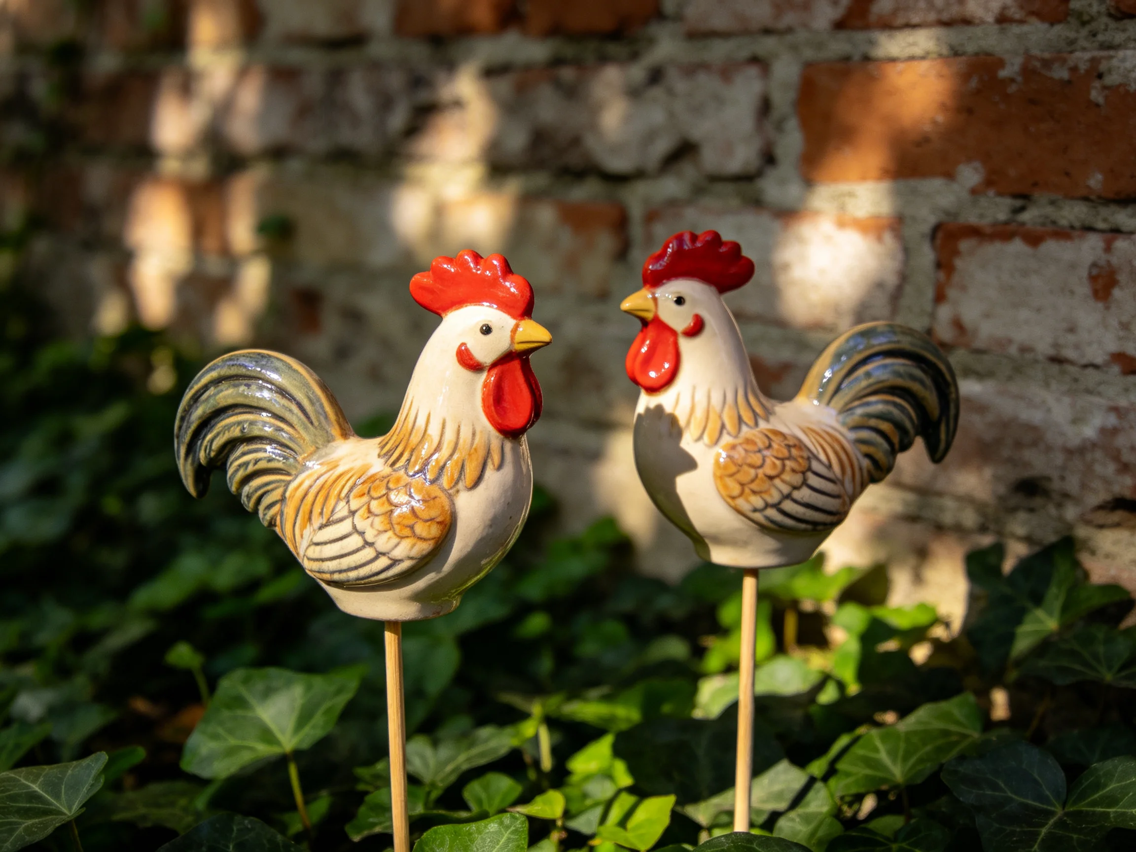 Two ceramic rooster figurines with red combs by a weathered brick wall